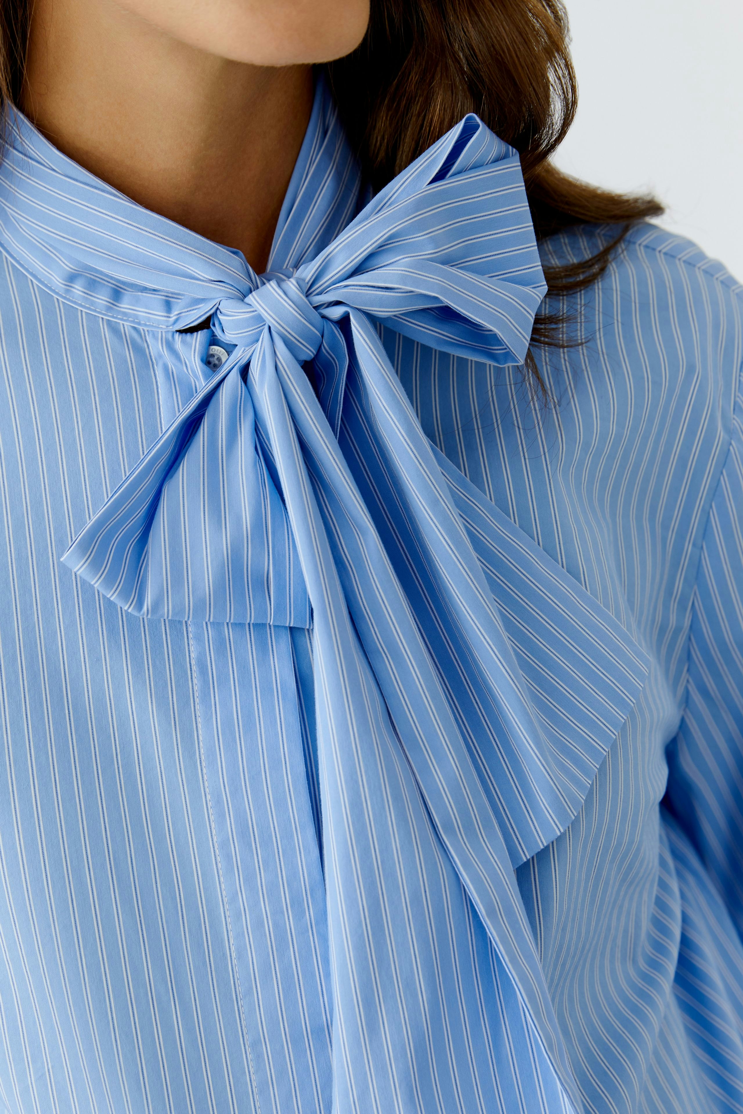 Stylish women's blouse: Close-up of a woman in a blue striped blouse with a large bow tie.