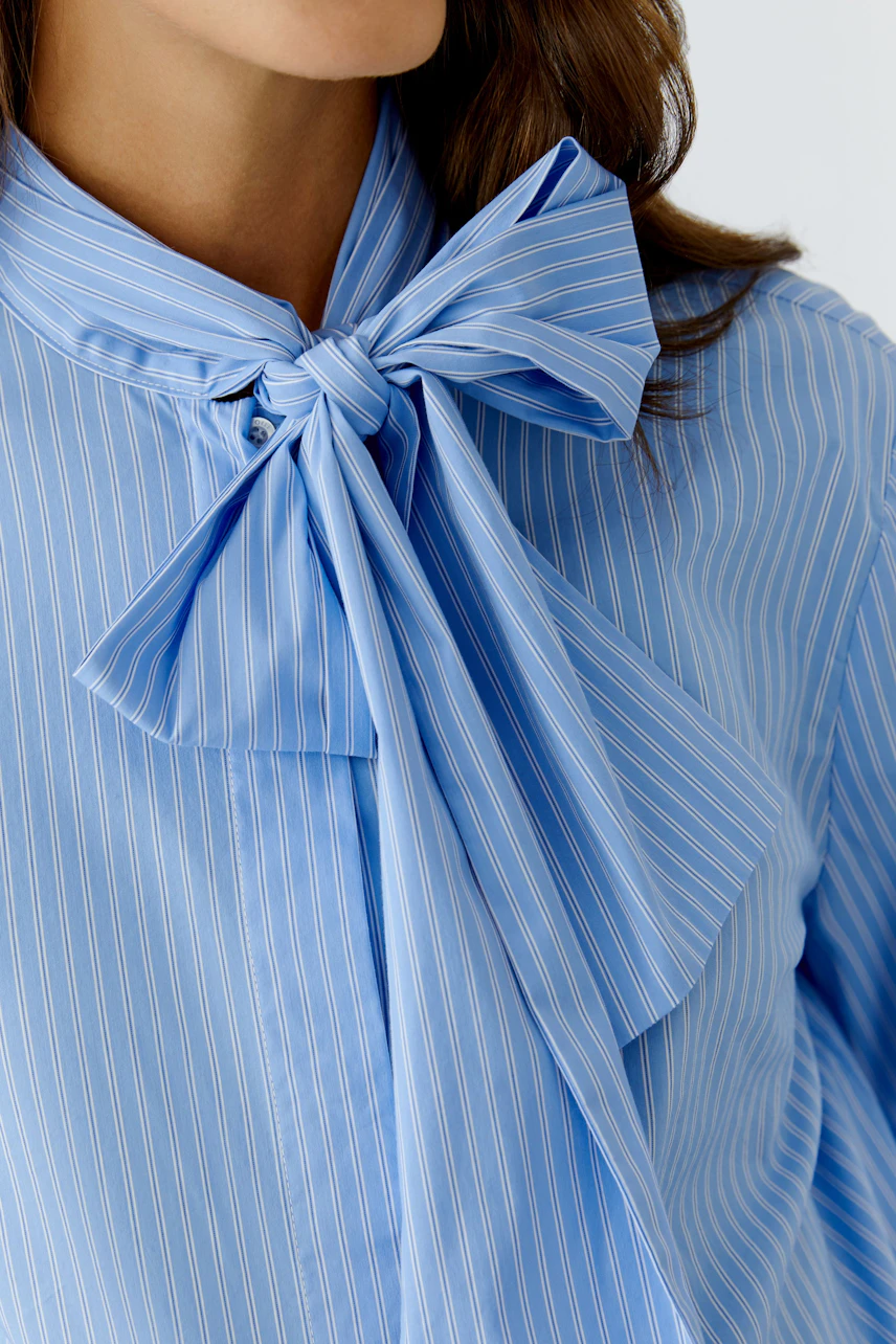 Stylish women's blouse: Close-up of a woman in a blue striped blouse with a large bow tie.