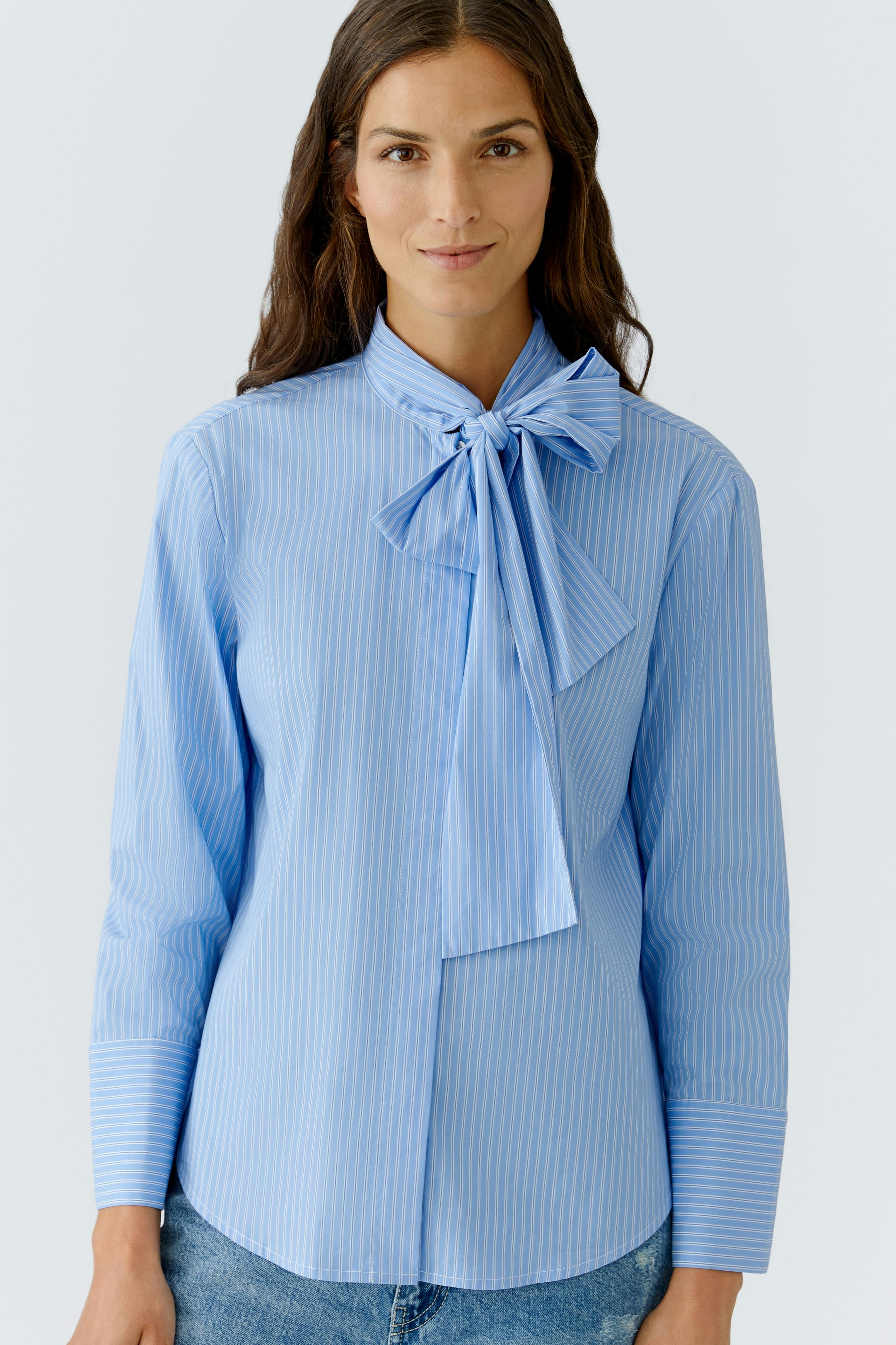 Stylish women's blouse: Woman in a light blue striped blouse with a bow tie detail.