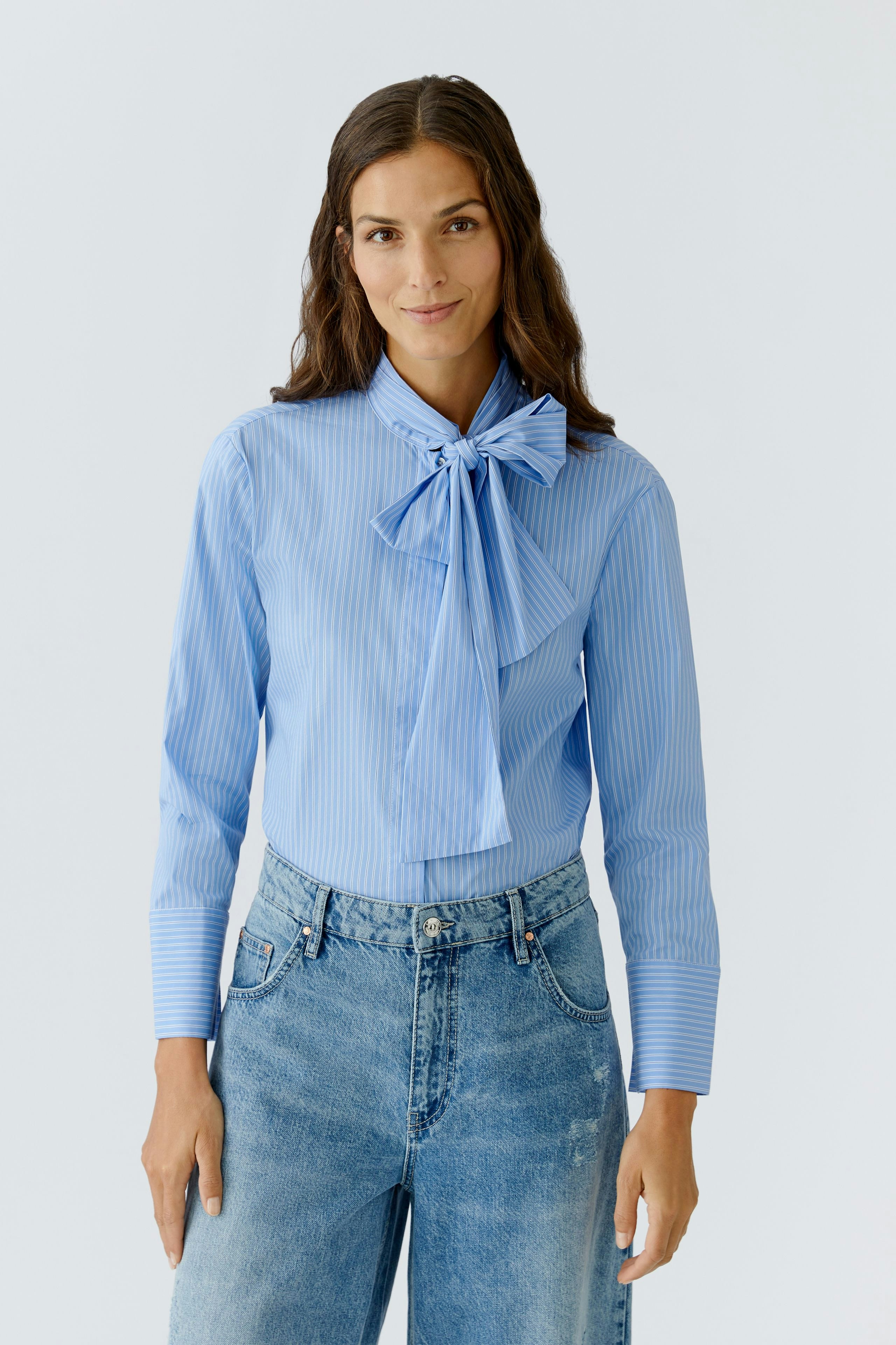 Stylish women's blouse: A woman in a light blue striped blouse with a bow, paired with casual jeans.