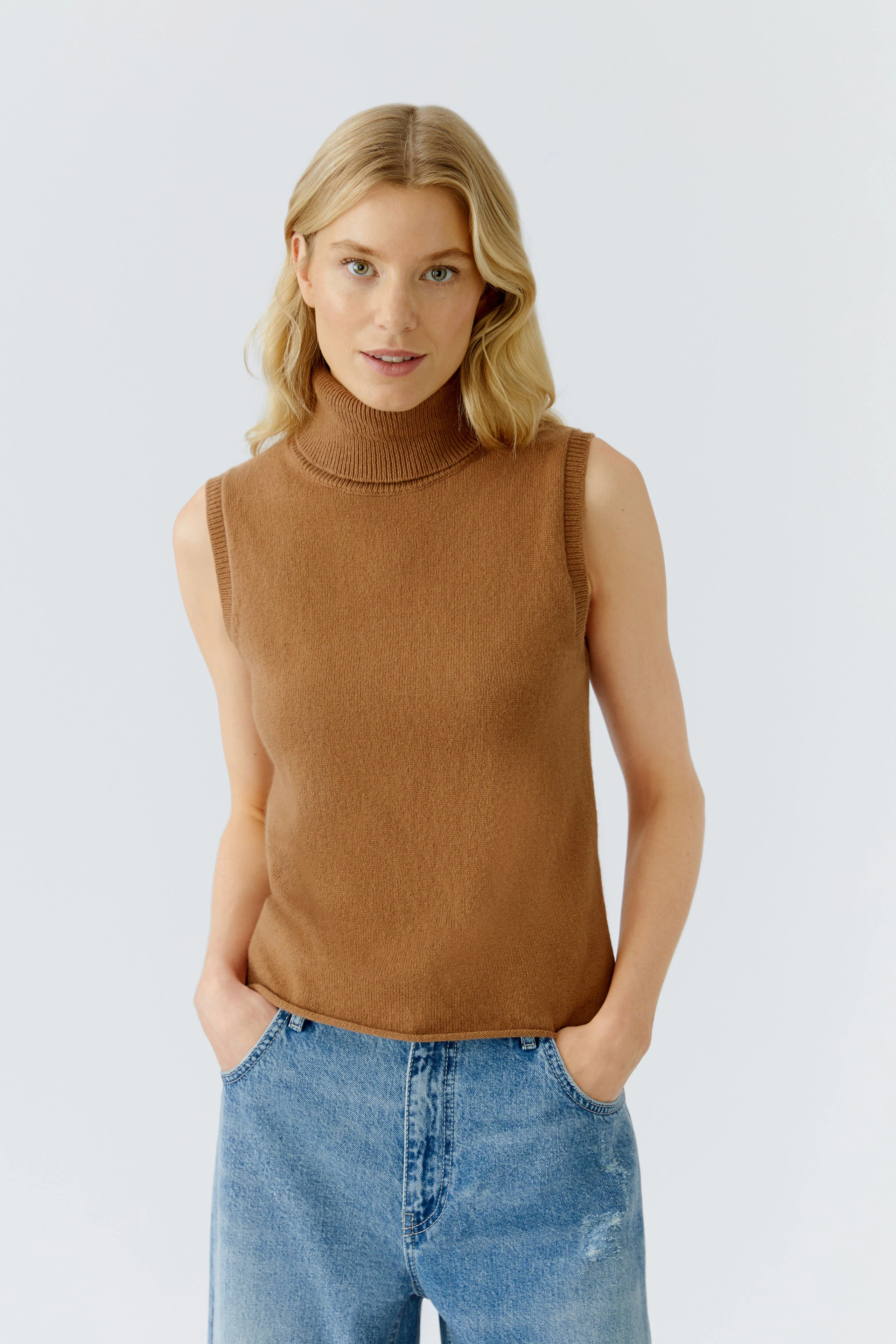 Beige Damen-Top mit Stehkragen: Frau trägt ein ärmelloses Oberteil und lässige Jeans.