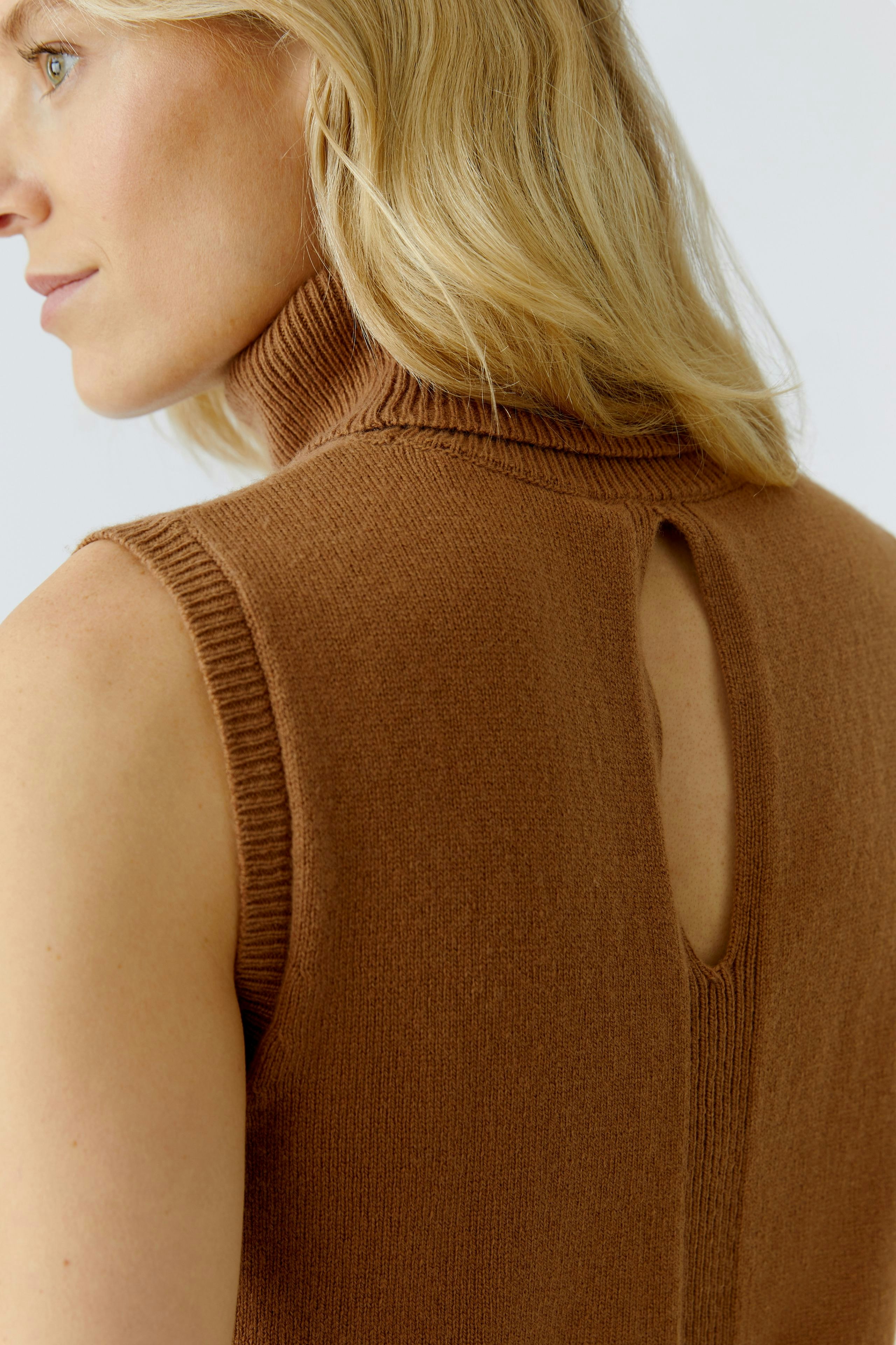 Stylish women's top: Close-up of a woman in a brown sleeveless top with a high neck and back keyhole detail.