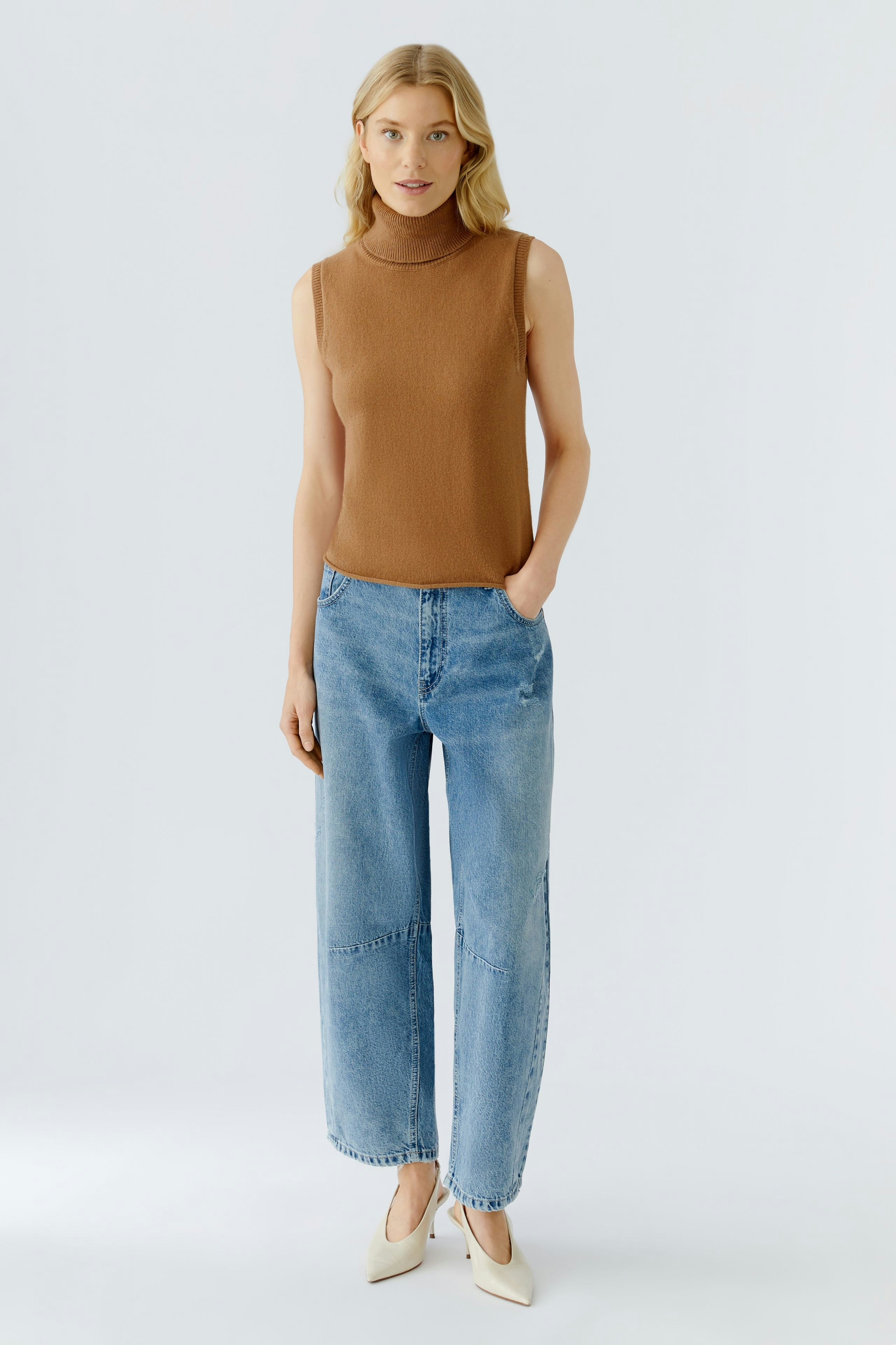 Casual women's top: A woman in a brown sleeveless top paired with wide blue jeans stands confidently.