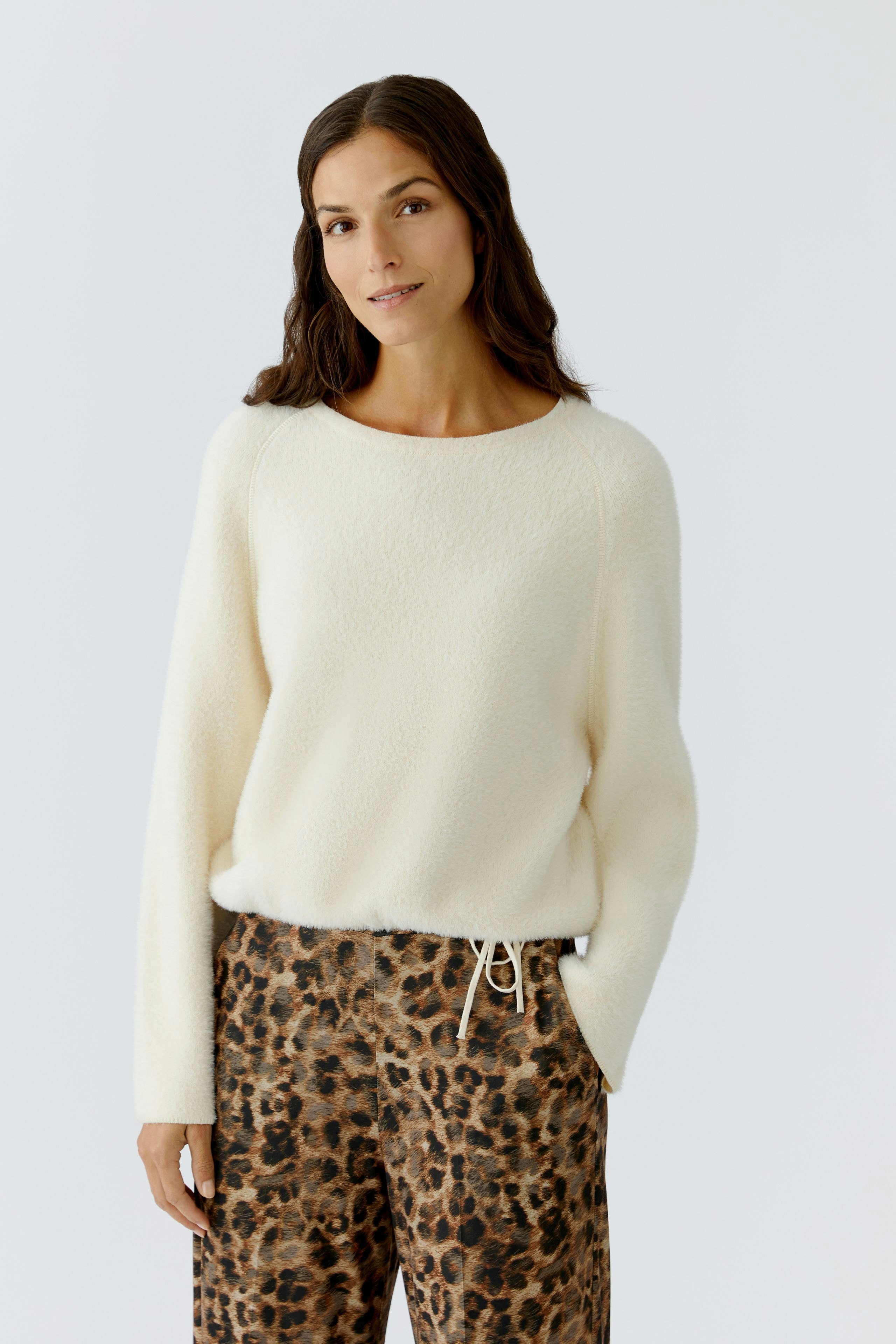 Damen-Pullover in Creme: Frau trägt einen weichen, lässigen Pullover mit Rundhalsausschnitt und lockerer Passform.