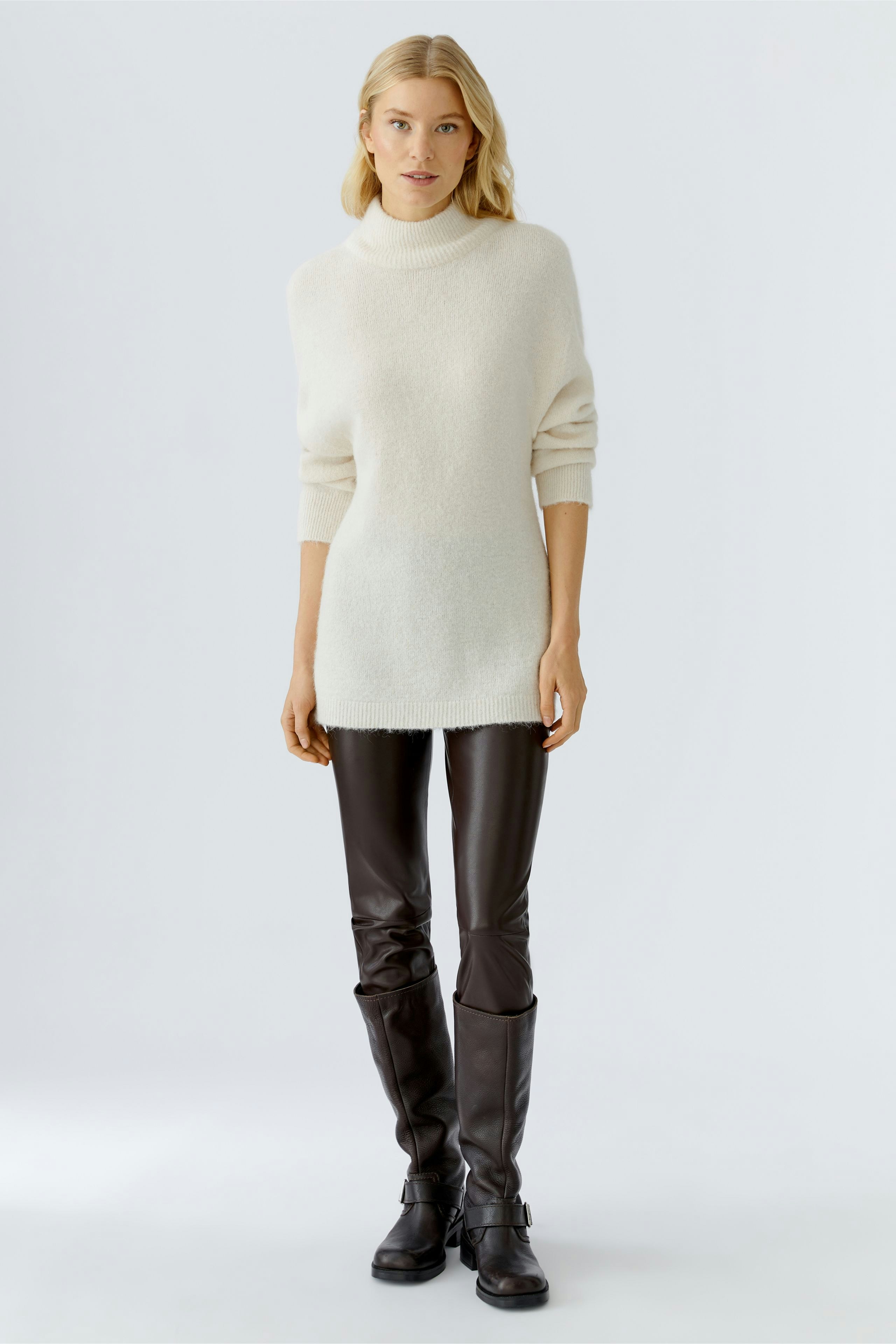 Cozy women's pullover in soft white, paired with brown leather pants for a relaxed look.