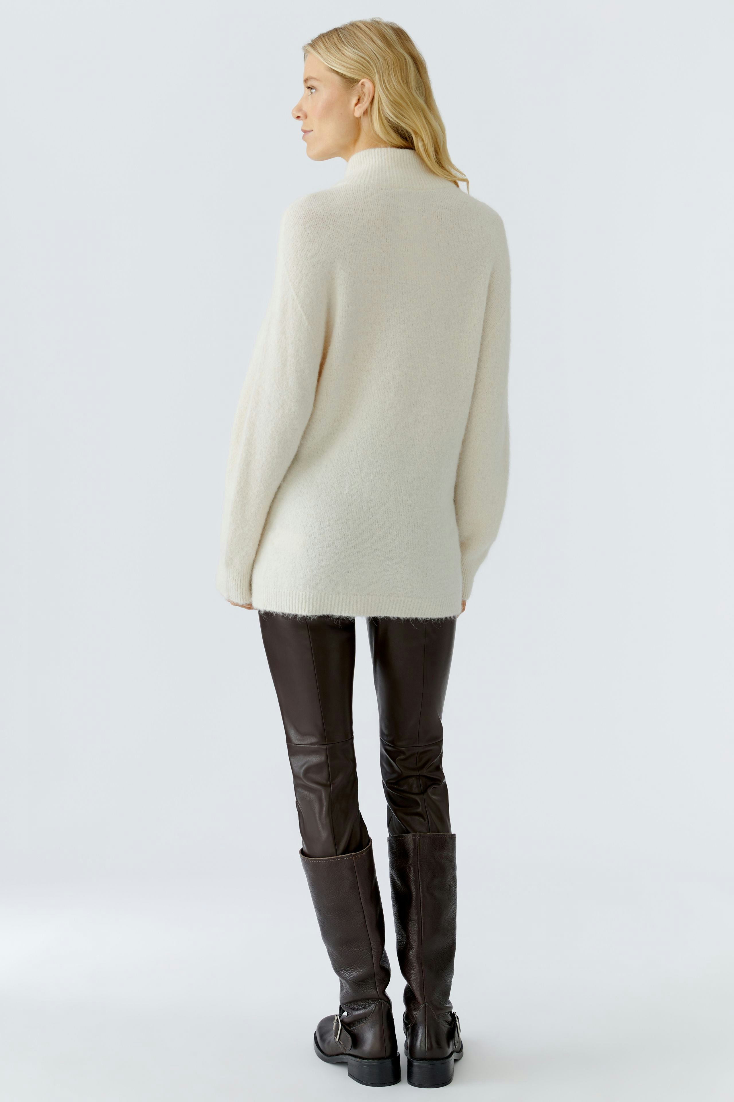 Cozy women's pullover: A woman in a soft cream pullover paired with brown leather pants.