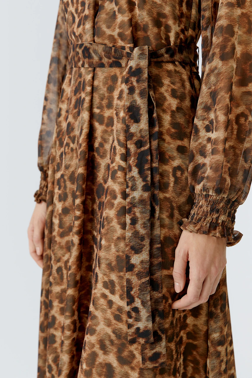 Maxikleid in Leo-Optik: Frau trägt ein luftiges, langes Kleid mit Taillengürtel und Rüschendetails.