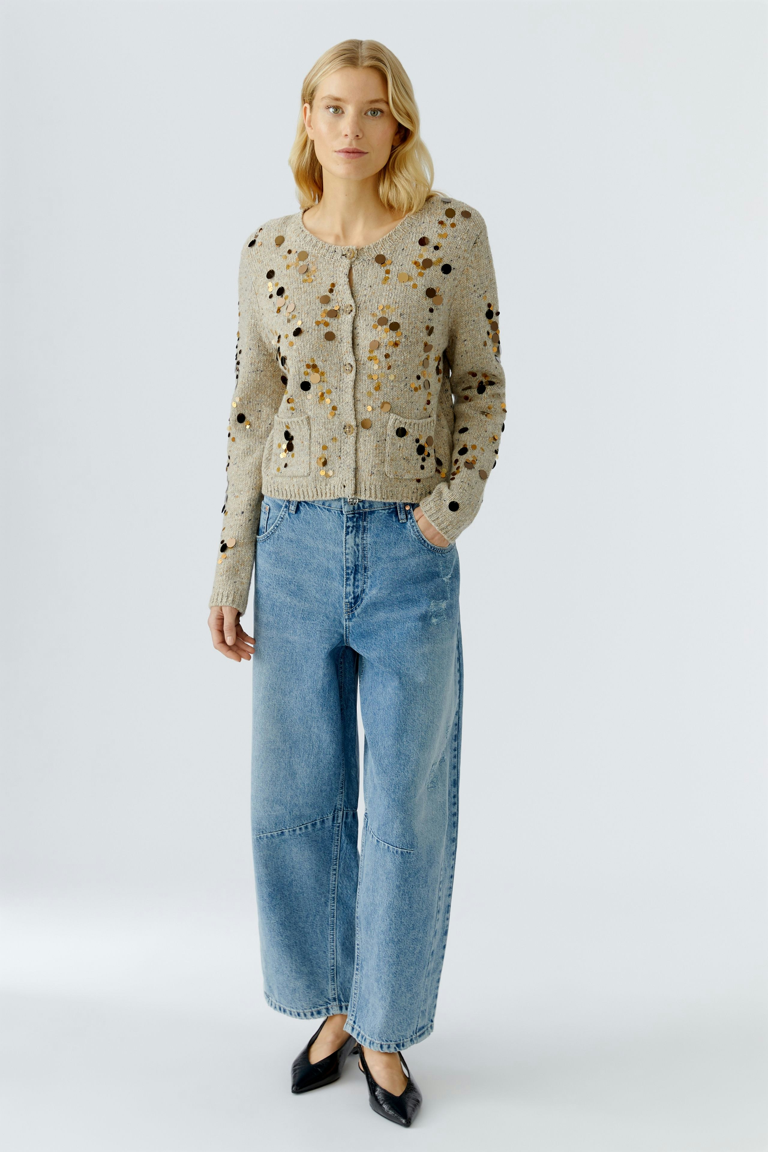 Casual women's cardigan: A woman in a beige cardigan with colorful details and relaxed-fit jeans.