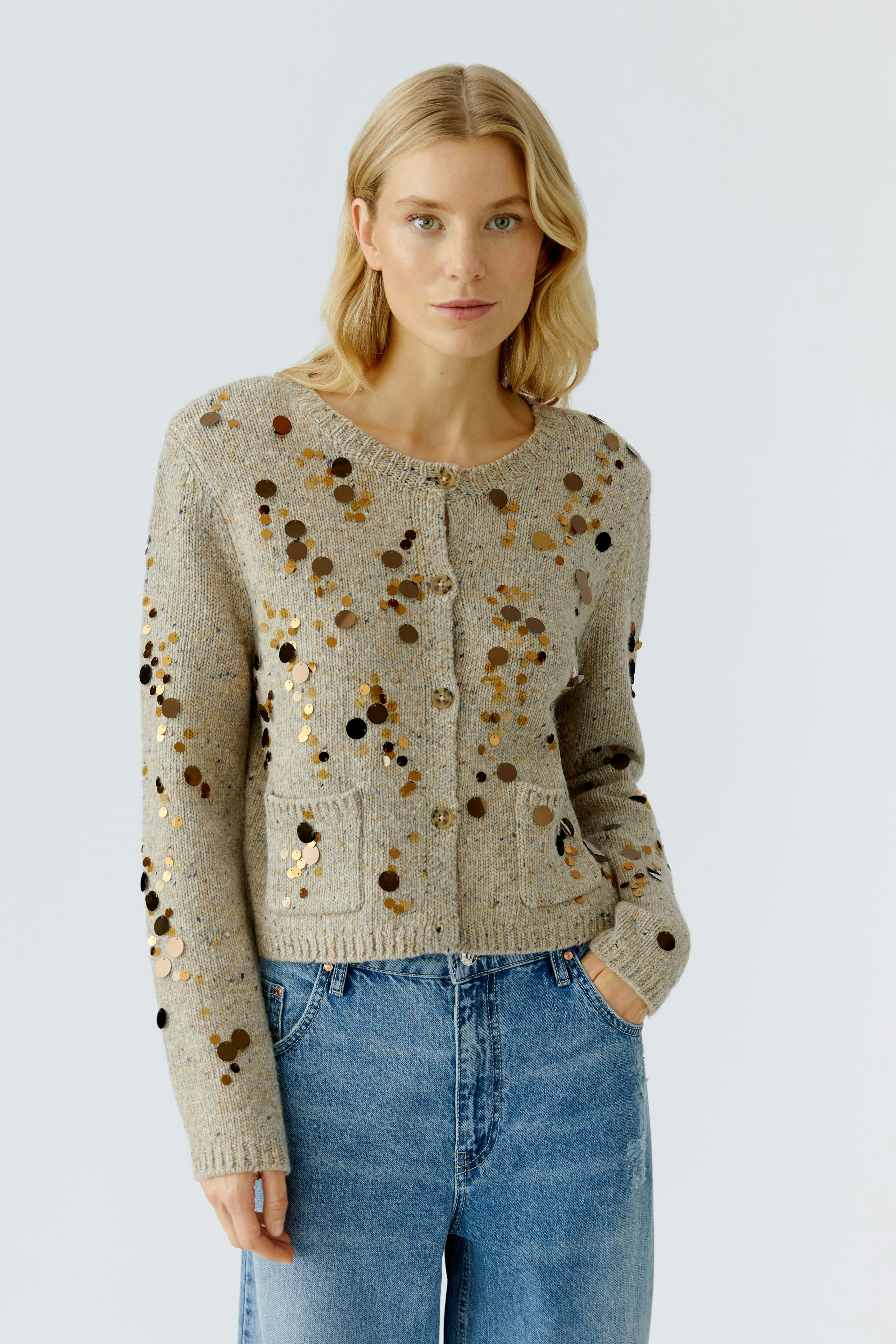 Casual women's cardigan: Young woman in a beige cardigan with sequins and pockets, paired with blue jeans.