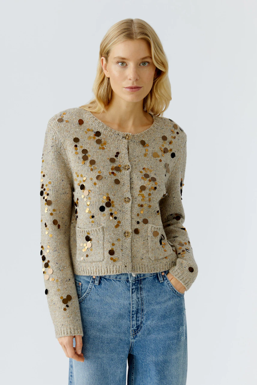 Casual women's cardigan: Young woman in a beige cardigan with sequins and pockets, paired with blue jeans.