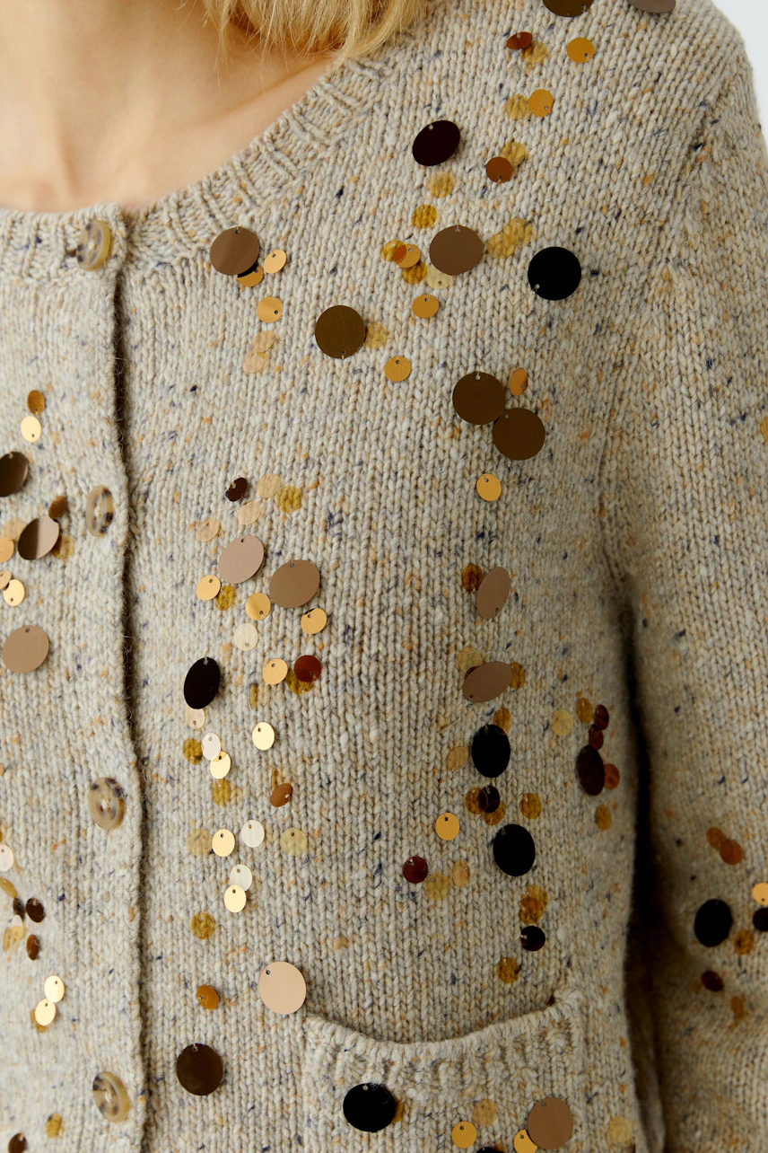 Casual women's cardigan: Close-up of a woman in a beige cardigan with sequins and pockets.