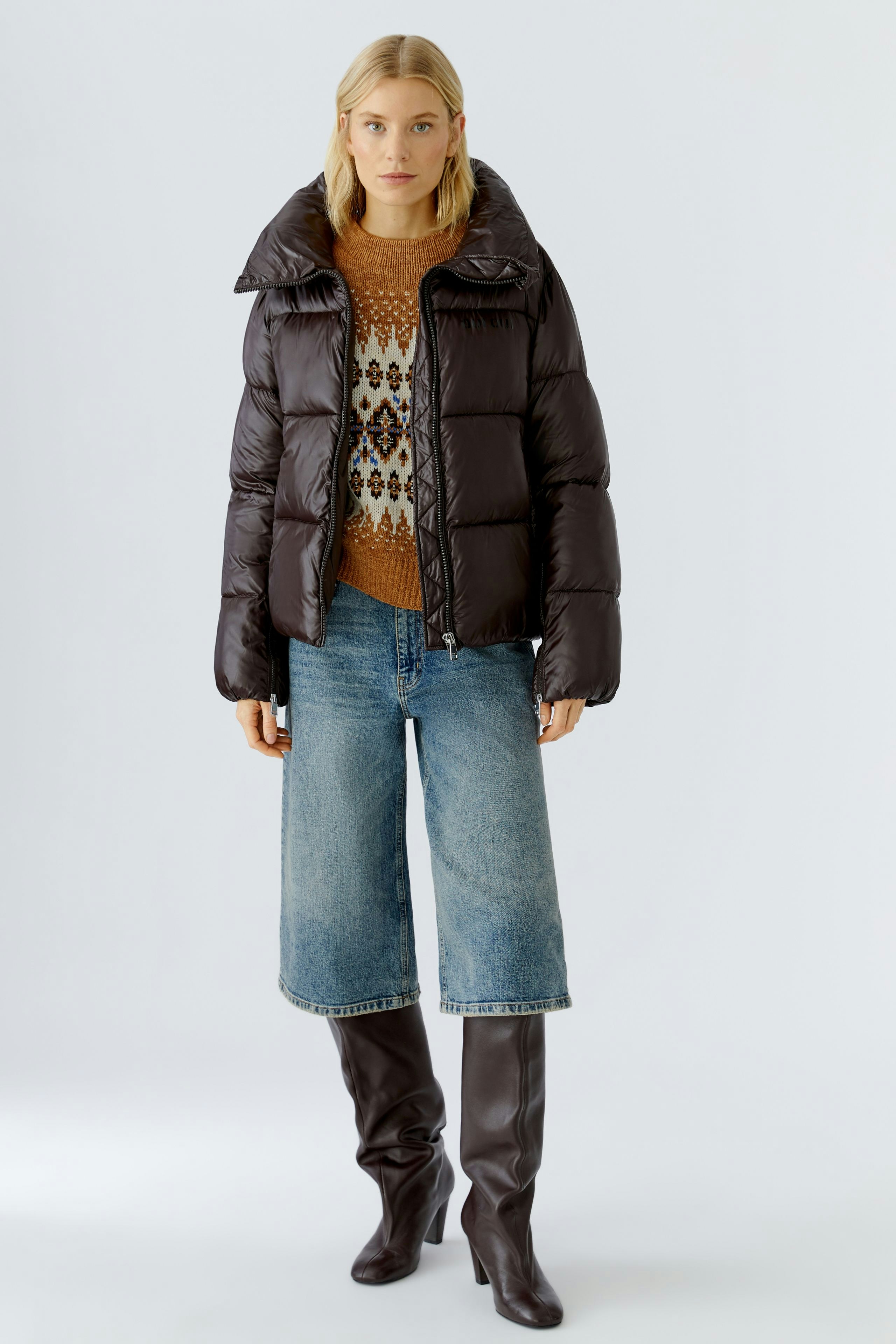 Stylish women's outdoor jacket: A woman in a puffy black jacket over a patterned pullover and jeans.