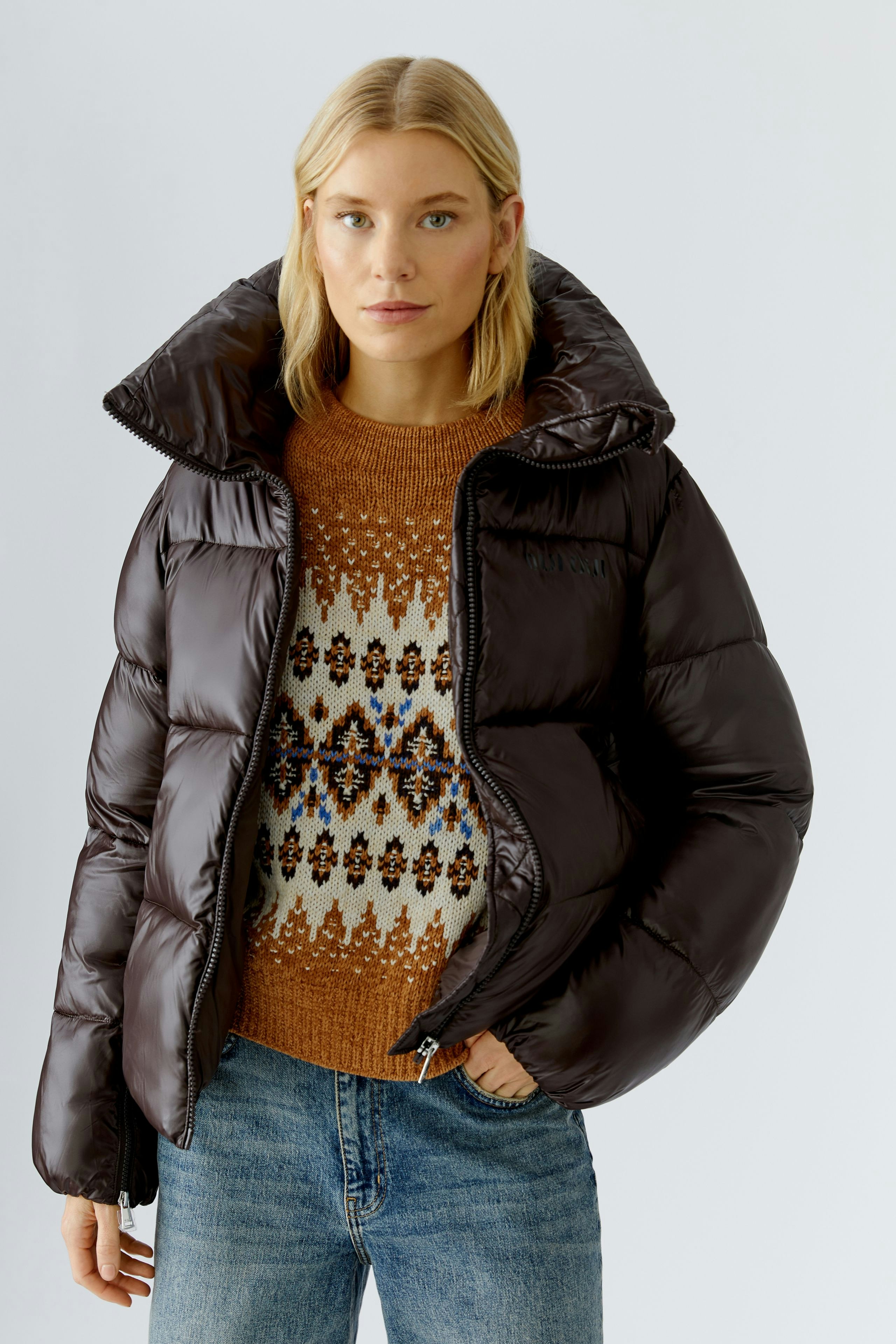 Stylish women's outdoor jacket: A woman in a brown puffer jacket over a patterned pullover, ready for the outdoors.