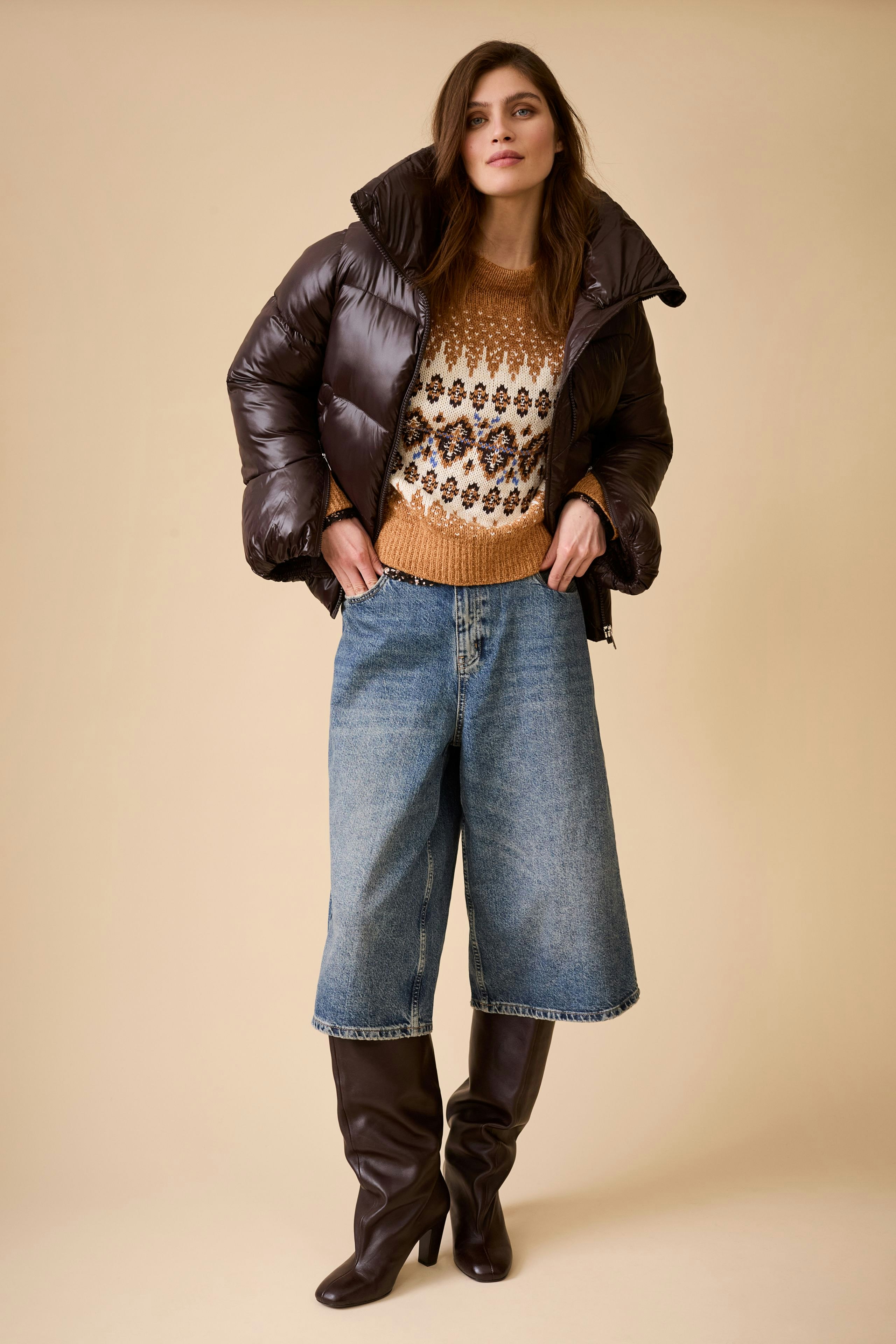 Stylish women's outdoor jacket: A woman in a brown puffer jacket over a patterned pullover and wide jeans.