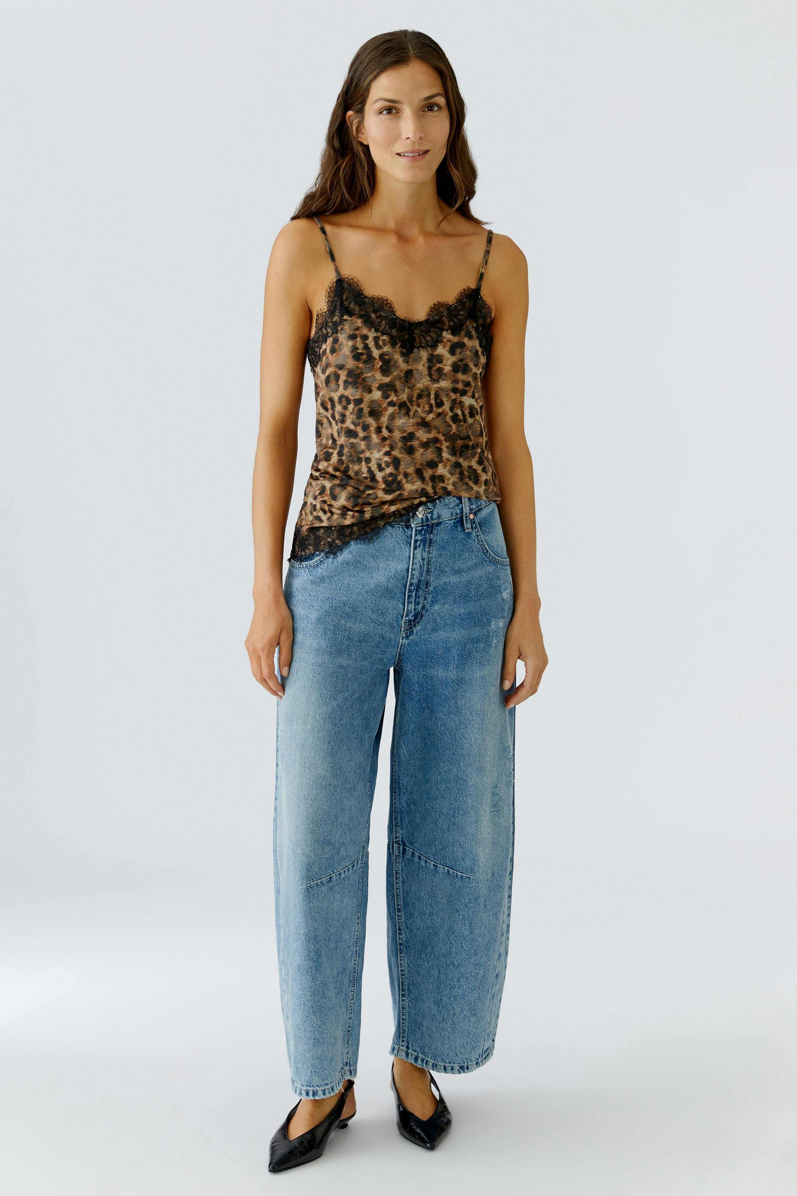 Stylish women's top: A woman in a leopard print camisole with lace details, paired with relaxed jeans.