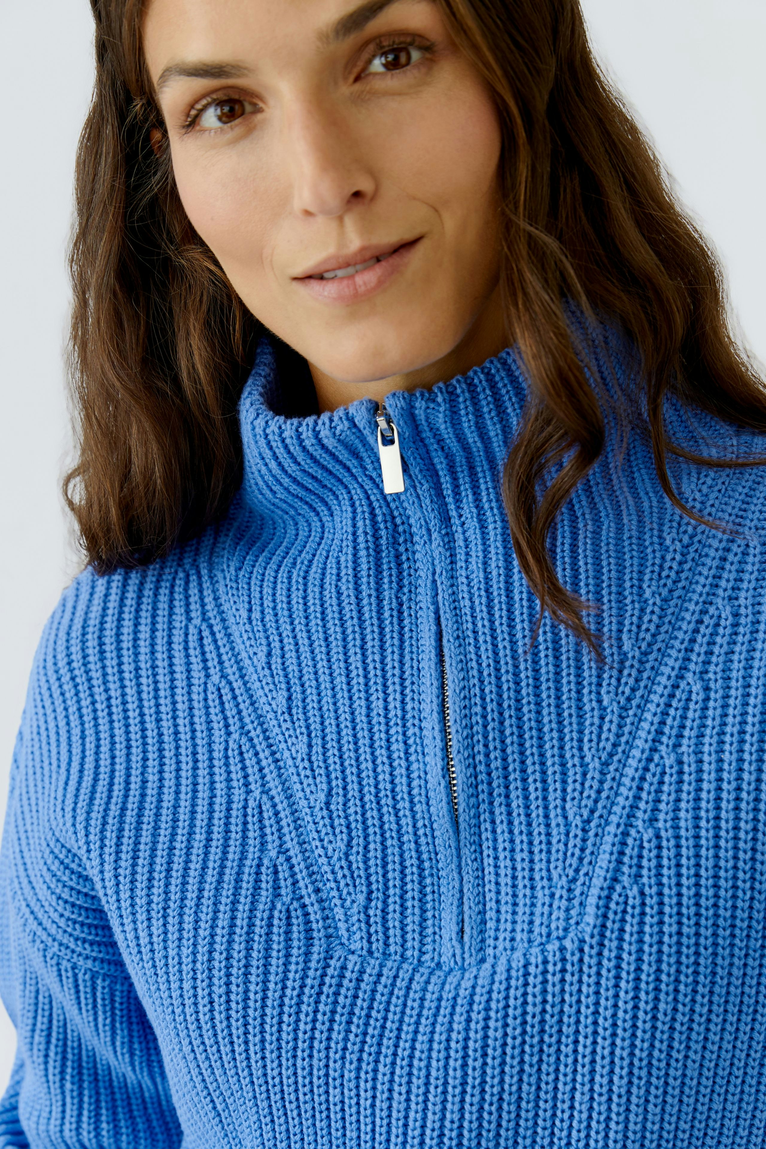 Casual women's pullover: Woman in a blue knitted pullover with a zip collar, smiling confidently.