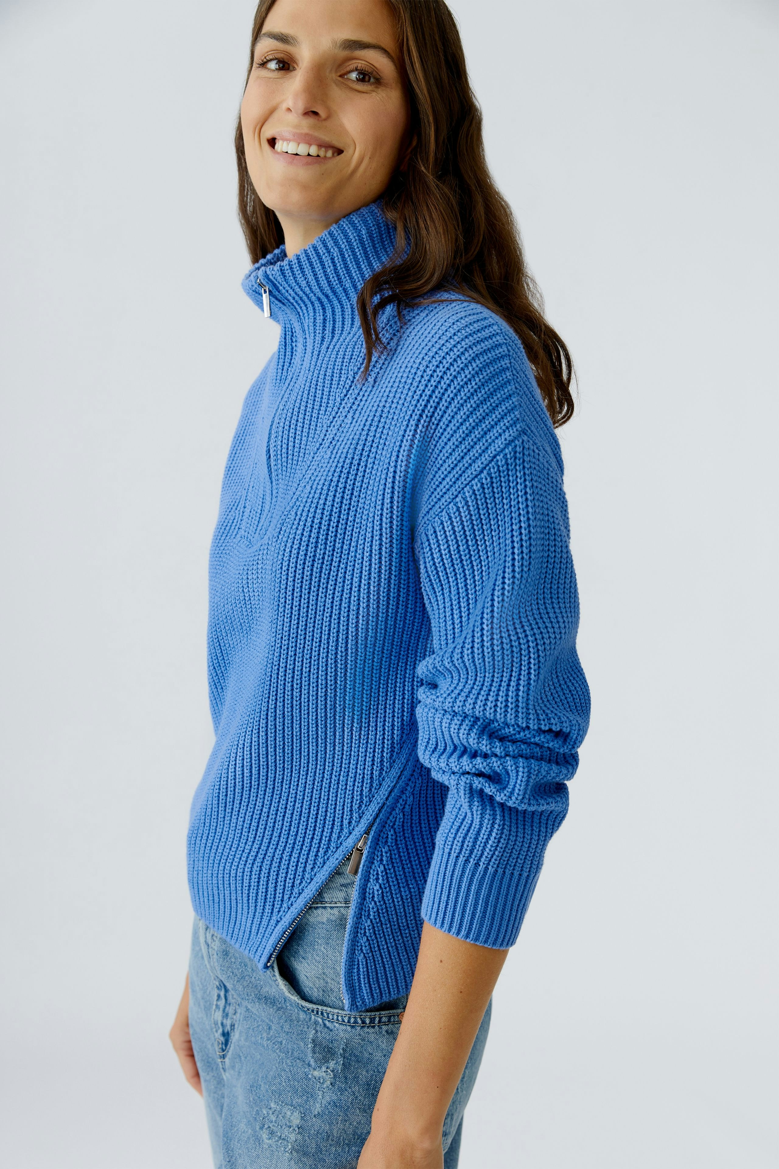 Casual women's pullover: Smiling woman in a blue knit pullover with a high collar and side slits.