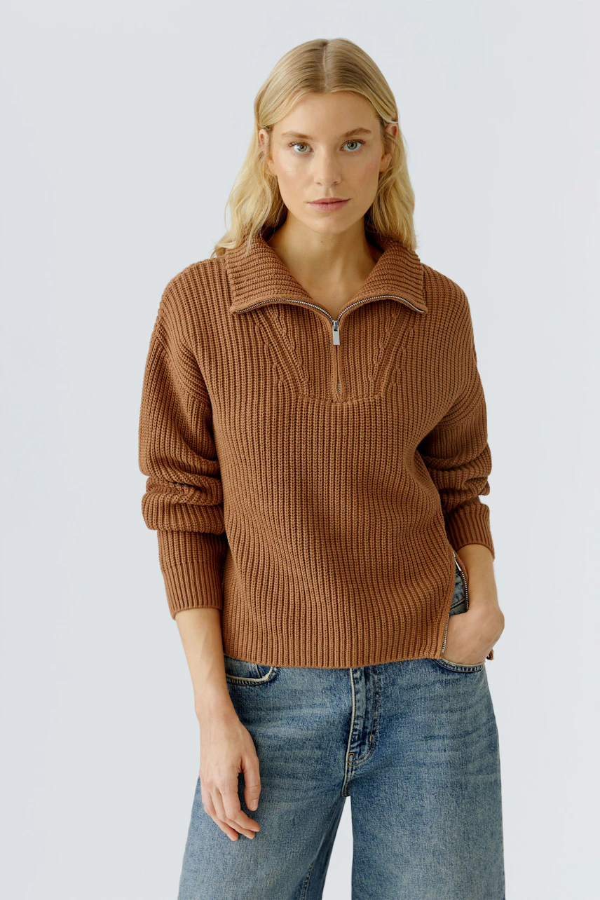 Casual women's pullover: A woman in a brown ribbed pullover with a zip collar, paired with jeans.