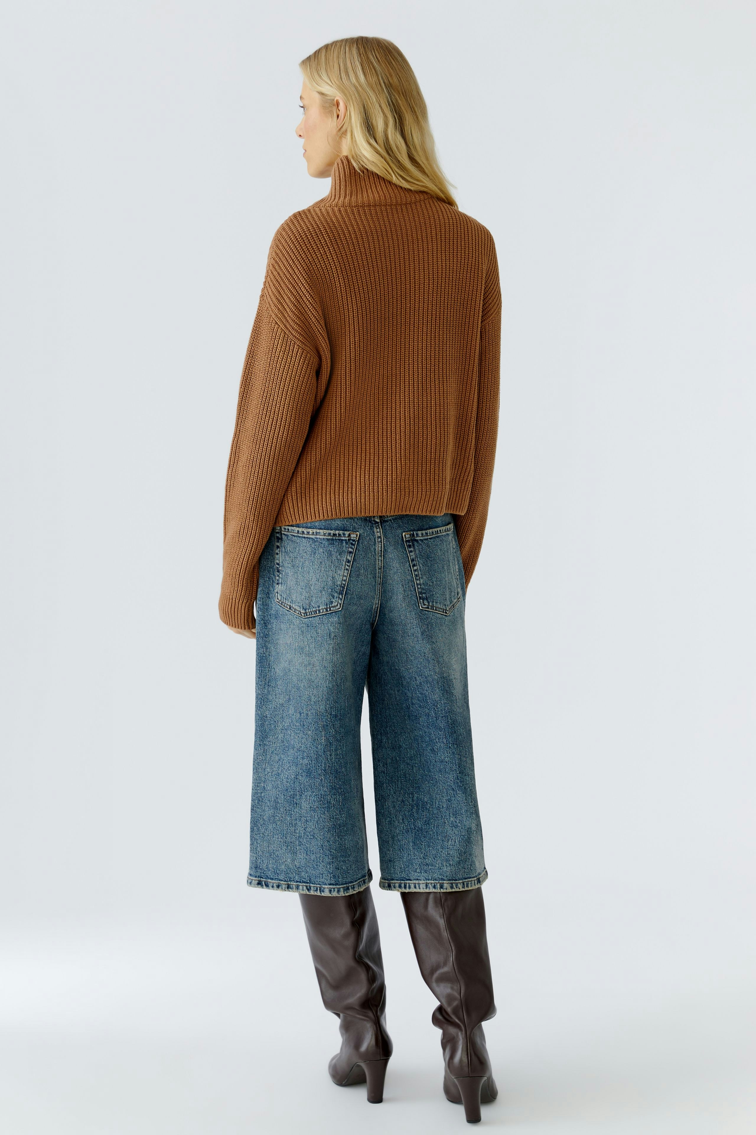 Casual women's pullover: A woman in a brown ribbed pullover paired with wide jeans and knee-high boots.