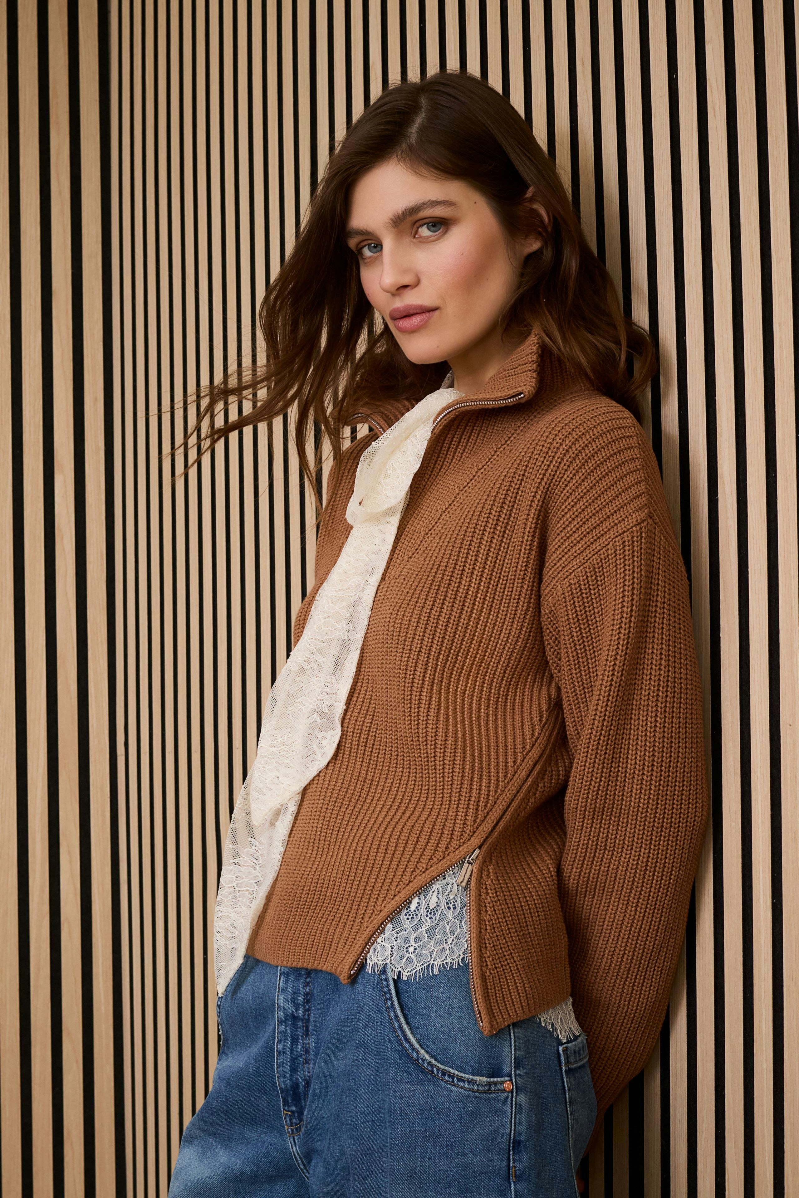 Casual women's pullover: Young woman in a brown ribbed pullover layered over a white top, styled with denim.