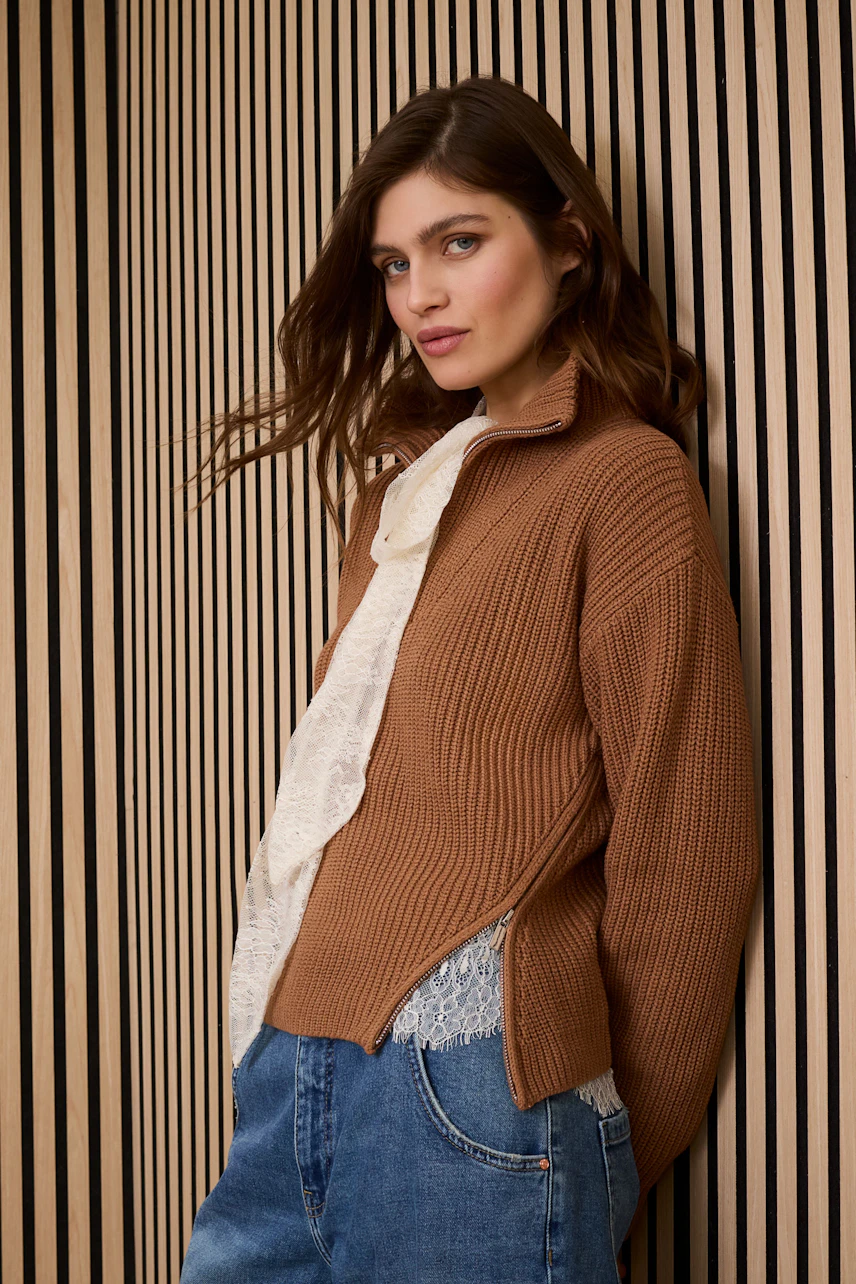 Casual women's pullover: Young woman in a brown ribbed pullover layered over a white top, styled with denim.