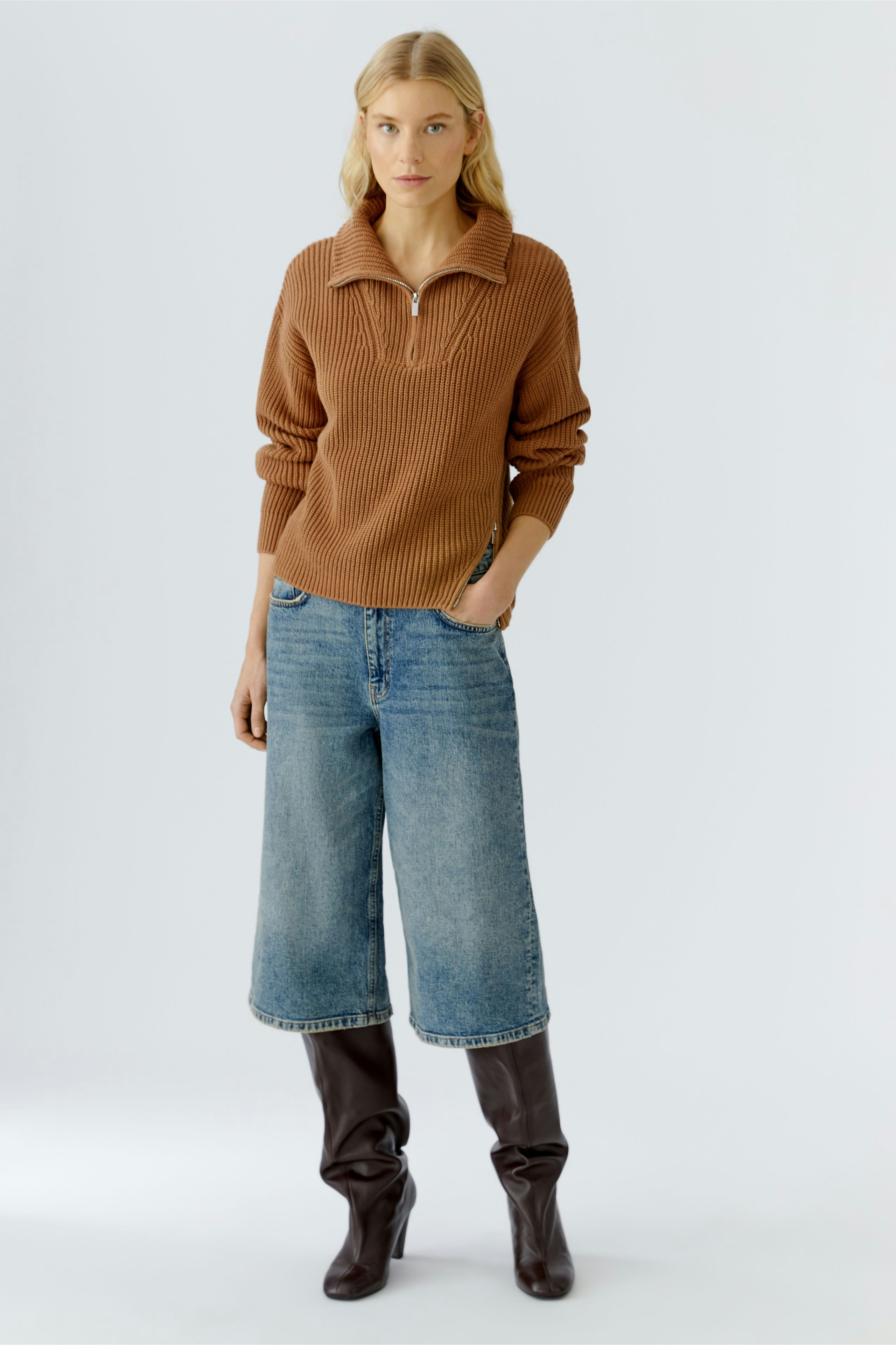 Casual women's pullover: Young woman in a brown ribbed pullover with a zip collar and relaxed fit jeans.