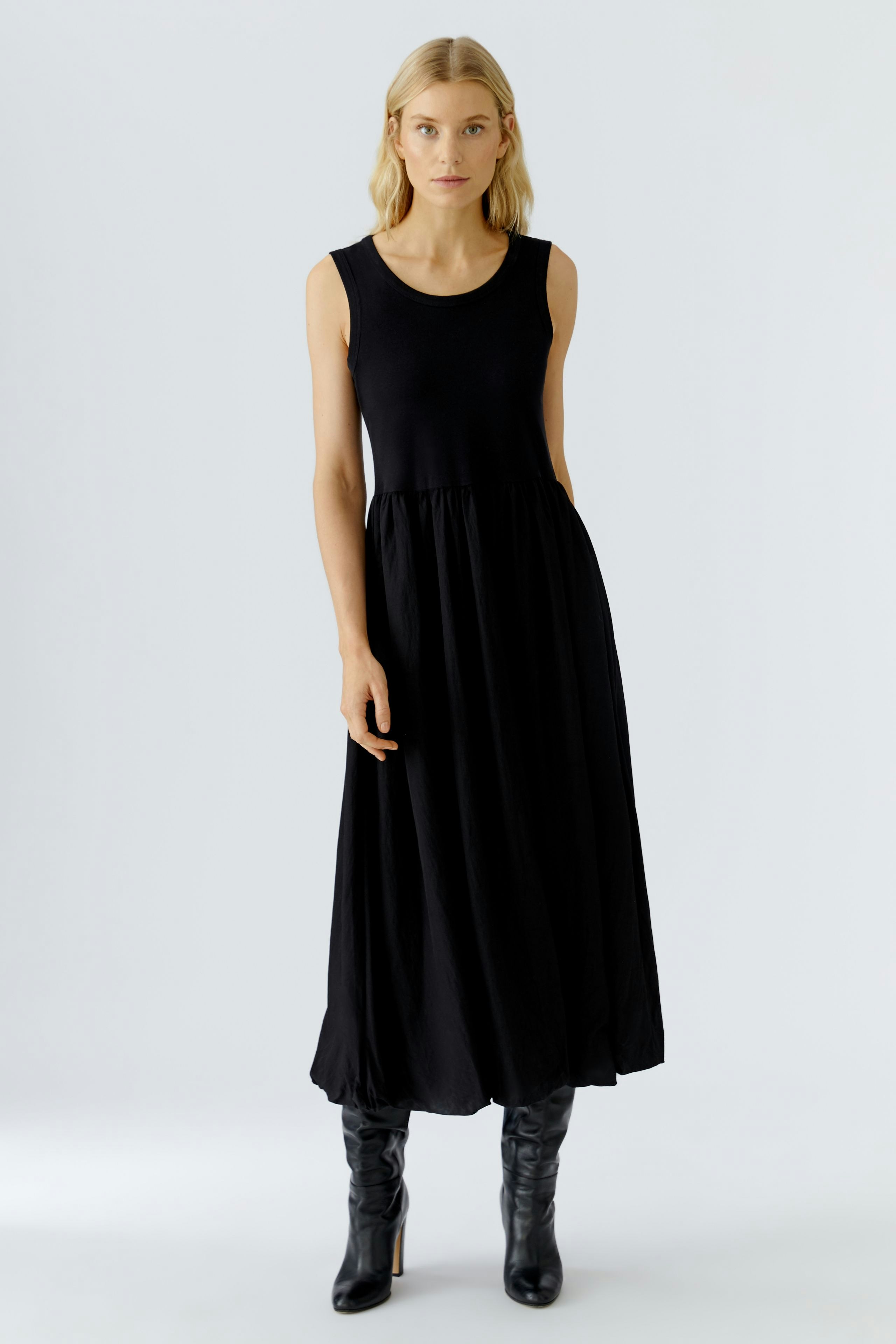 Casual black midi dress: Woman in a sleeveless, flowing design, paired with stylish knee-high boots.