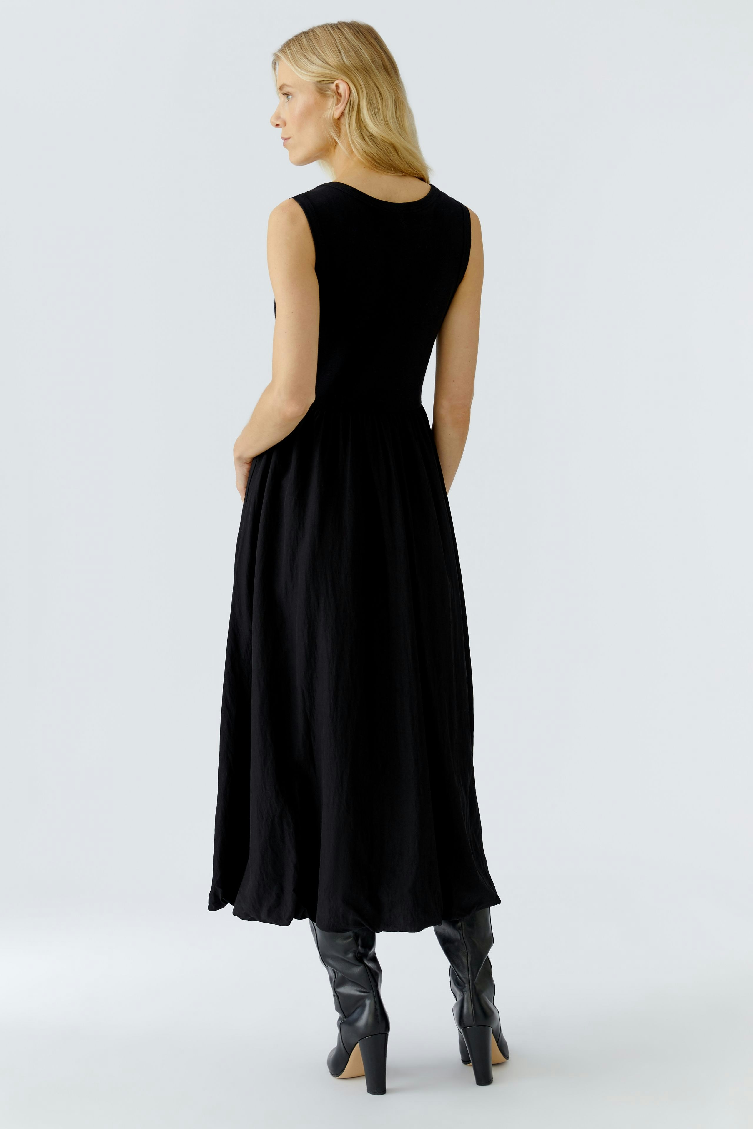 Casual black midi dress: Woman in a sleeveless dress with a flowing silhouette, paired with knee-high boots.