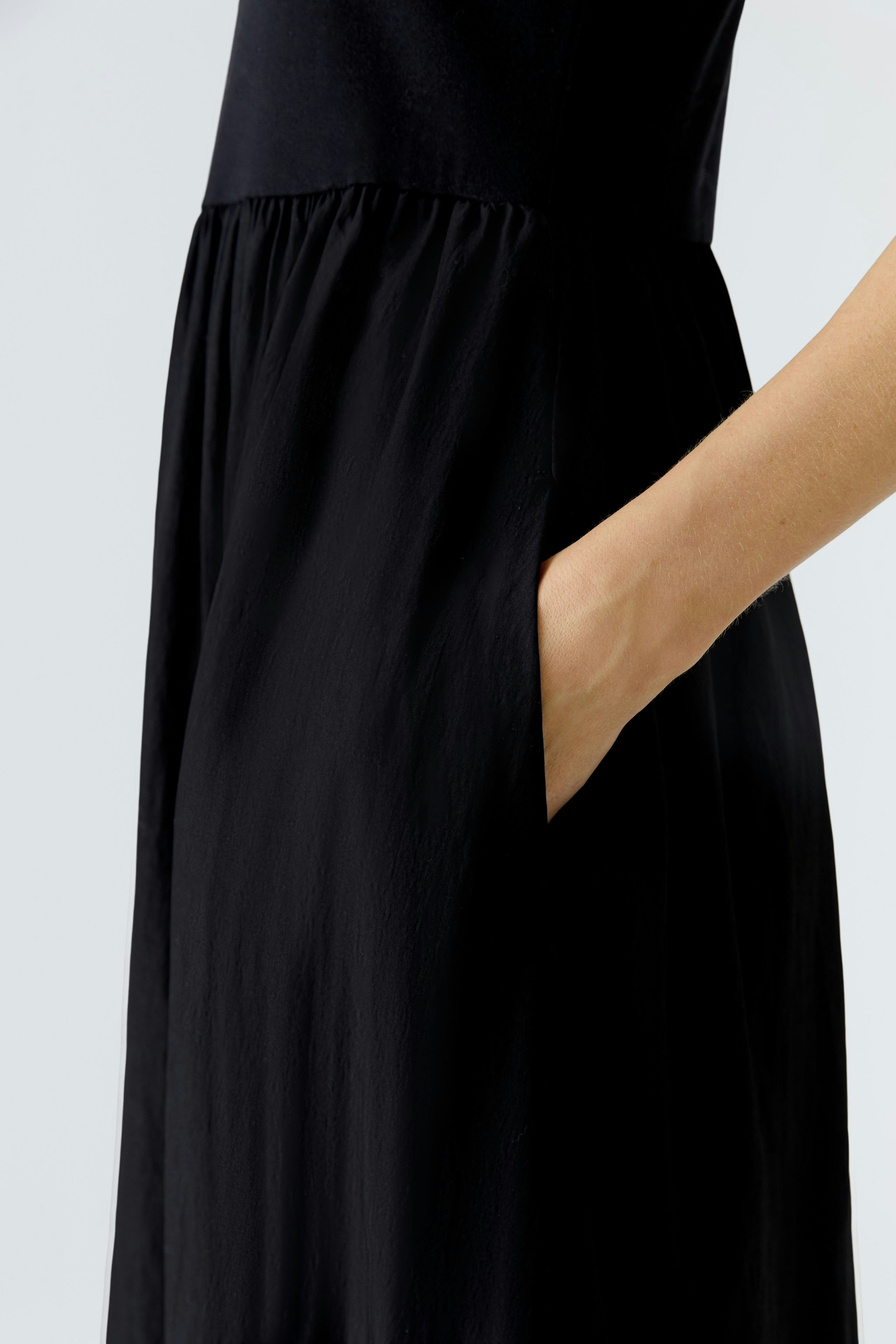 Casual black midi dress: Woman showing off the flowing fabric and practical side pockets.