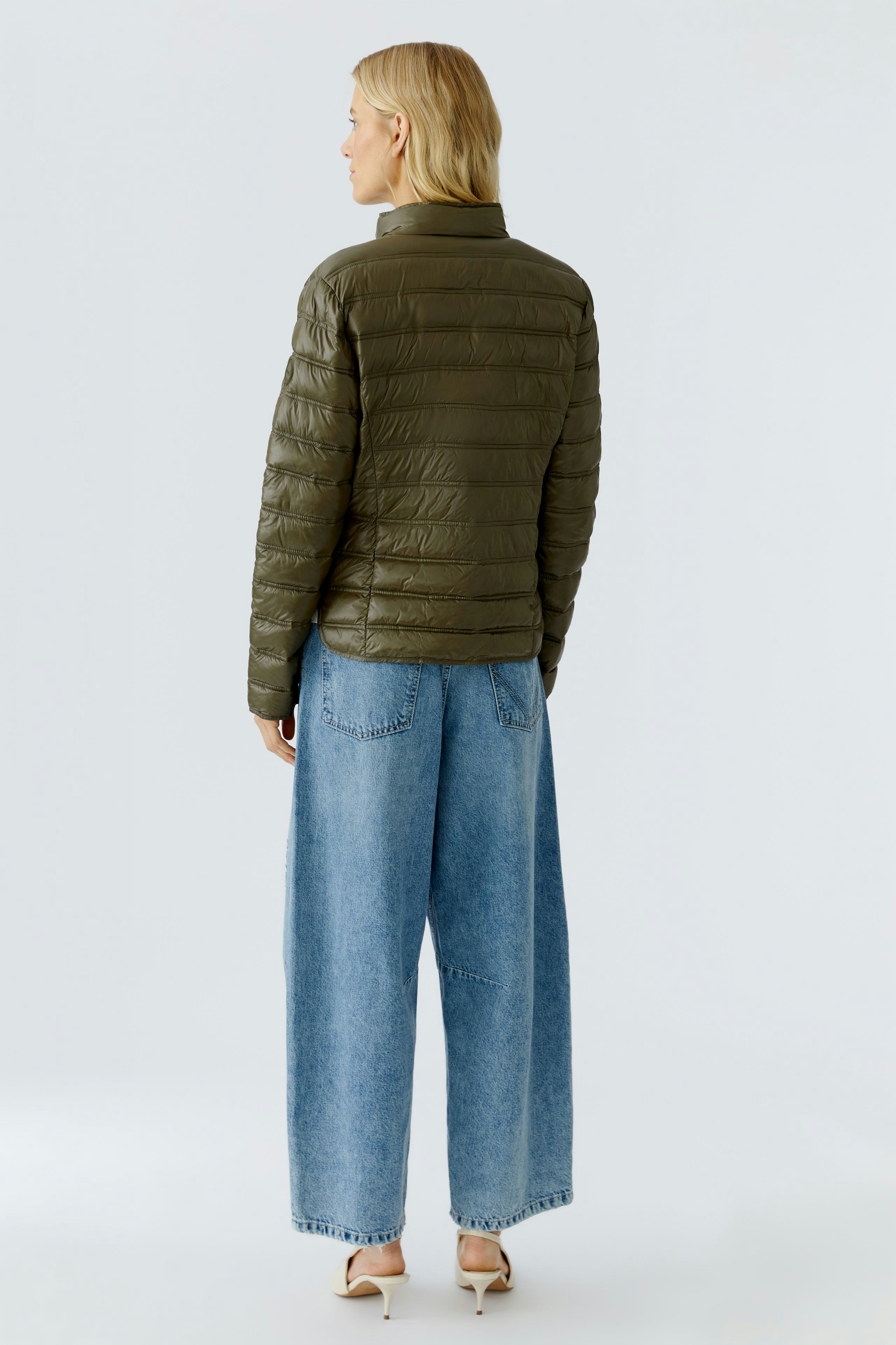 Lightweight outdoor jacket: Woman in olive green puffer jacket paired with wide-leg jeans.