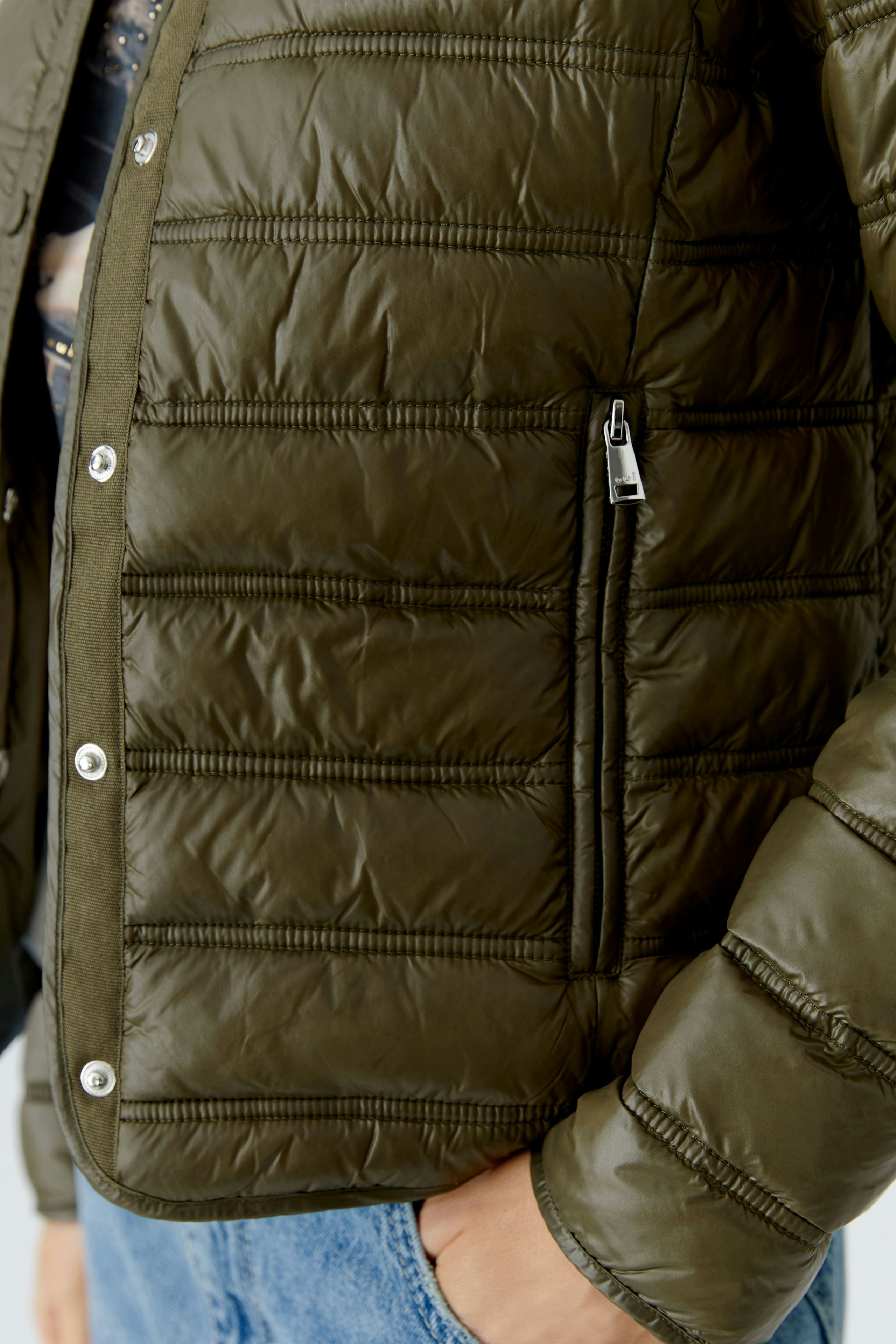 Casual women's outdoor jacket: Close-up of a woman in a green puffer jacket with zip pockets.