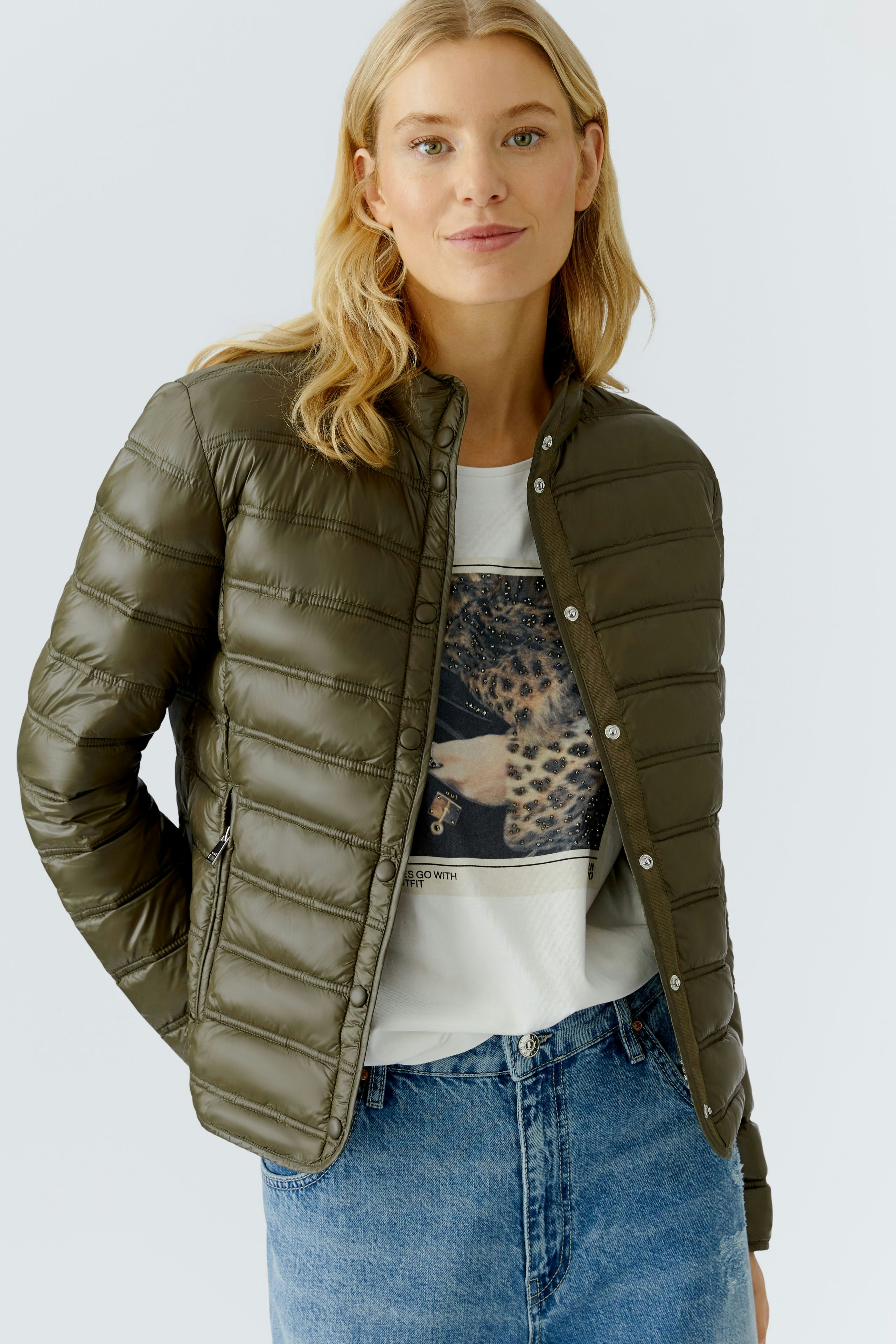 Lightweight outdoor jacket: Woman in a green puffer jacket over a graphic tee, smiling confidently.