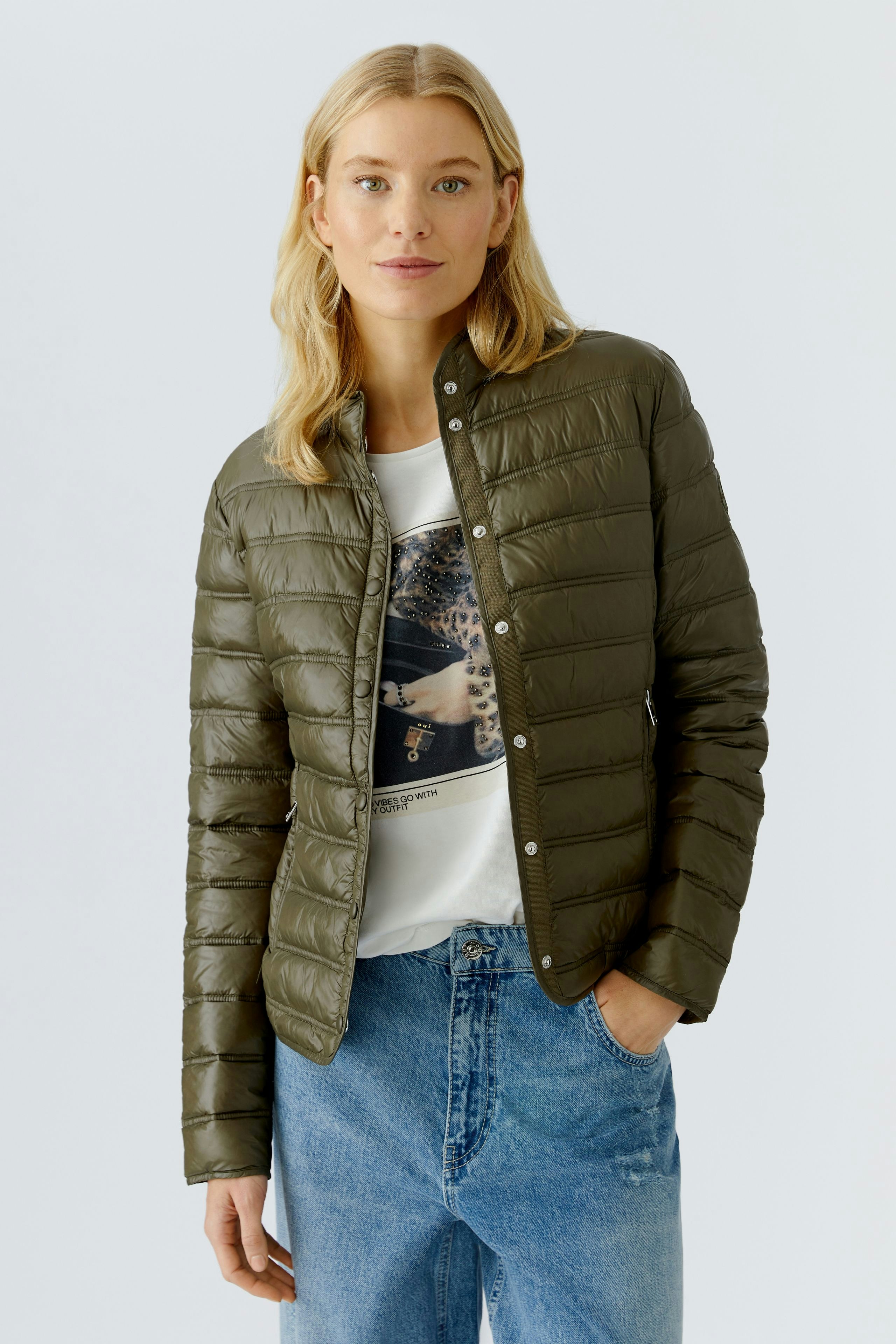 Lightweight outdoor jacket: Woman in a green puffer jacket over a graphic tee, paired with relaxed jeans.