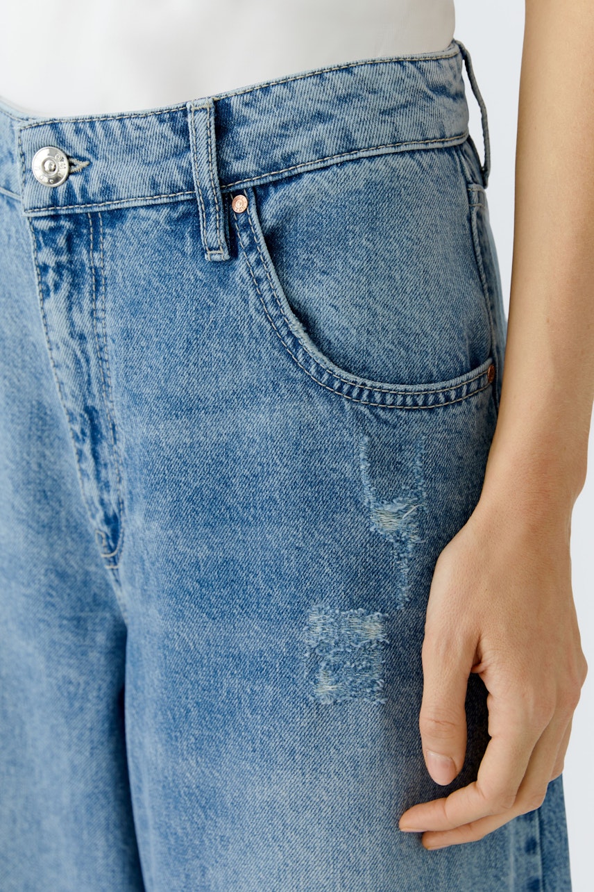 Bequeme Jeans Barrel: Frau trägt lässige, hellblaue Jeans mit lockerer Passform und modernen Details.
