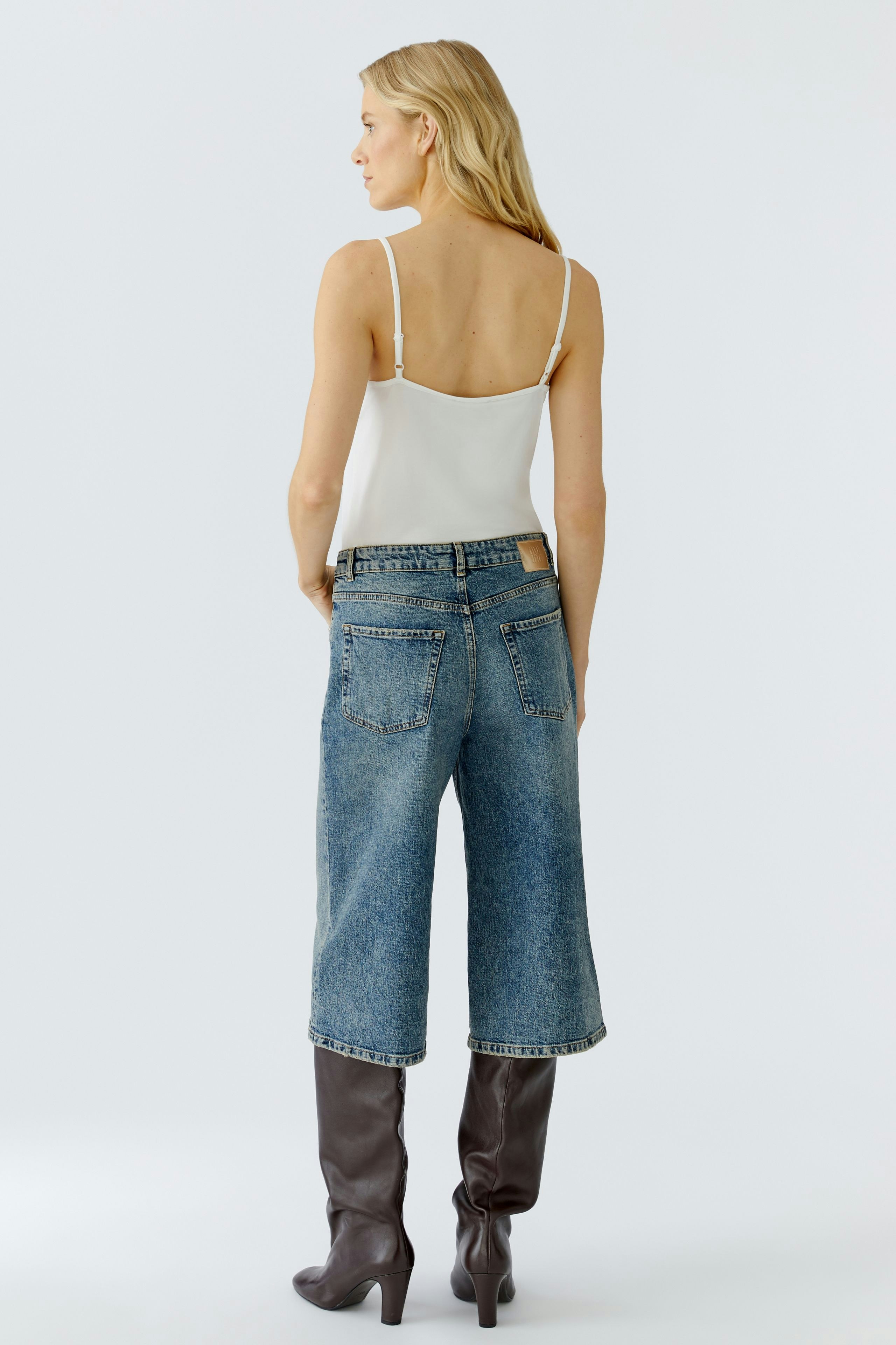 Casual women's jeans Bermuda: A woman in blue denim Bermuda shorts with a simple top and stylish boots.