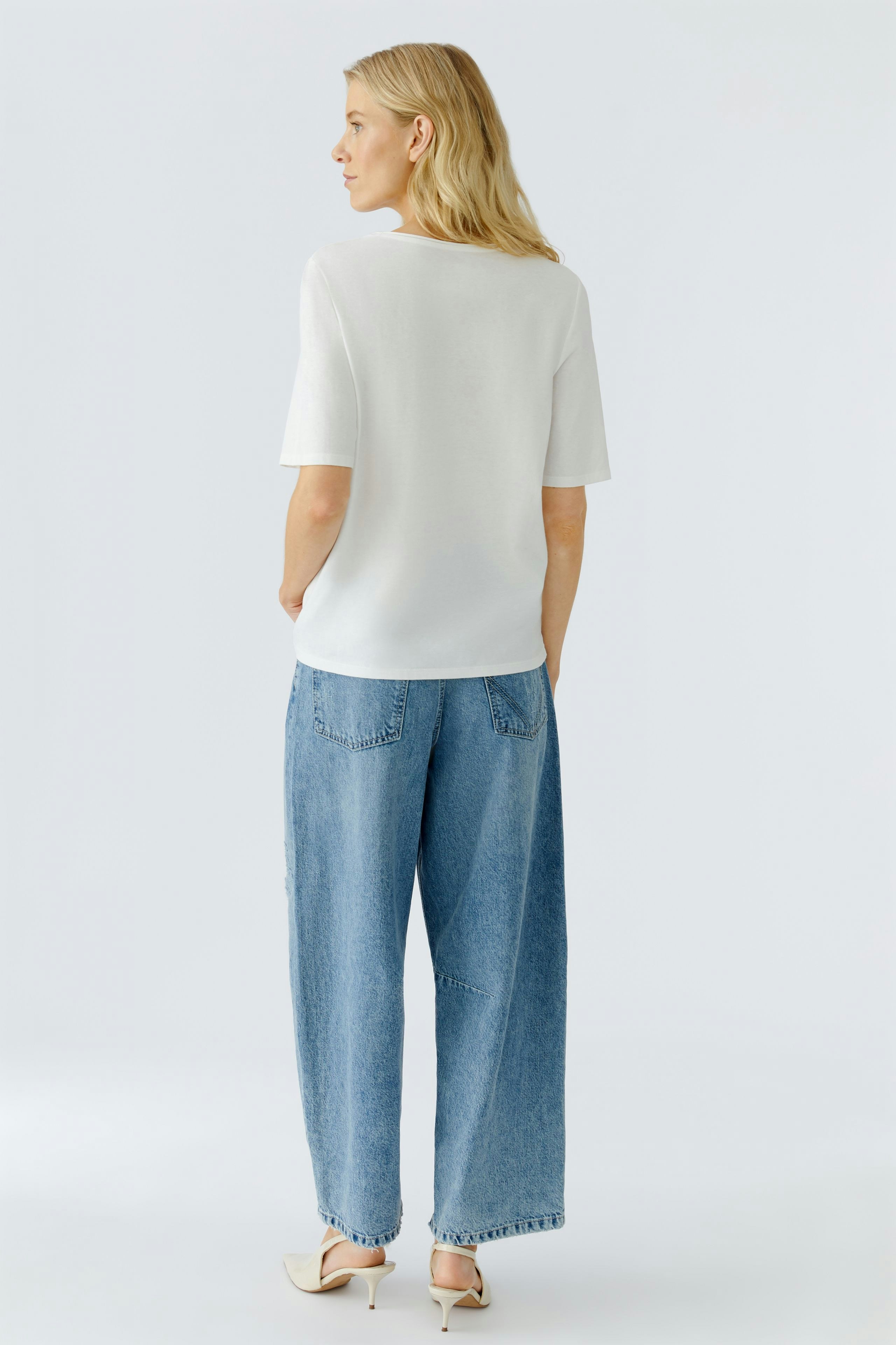 Casual women's T-shirt: Woman in a white top paired with relaxed-fit jeans, showcasing a simple style.