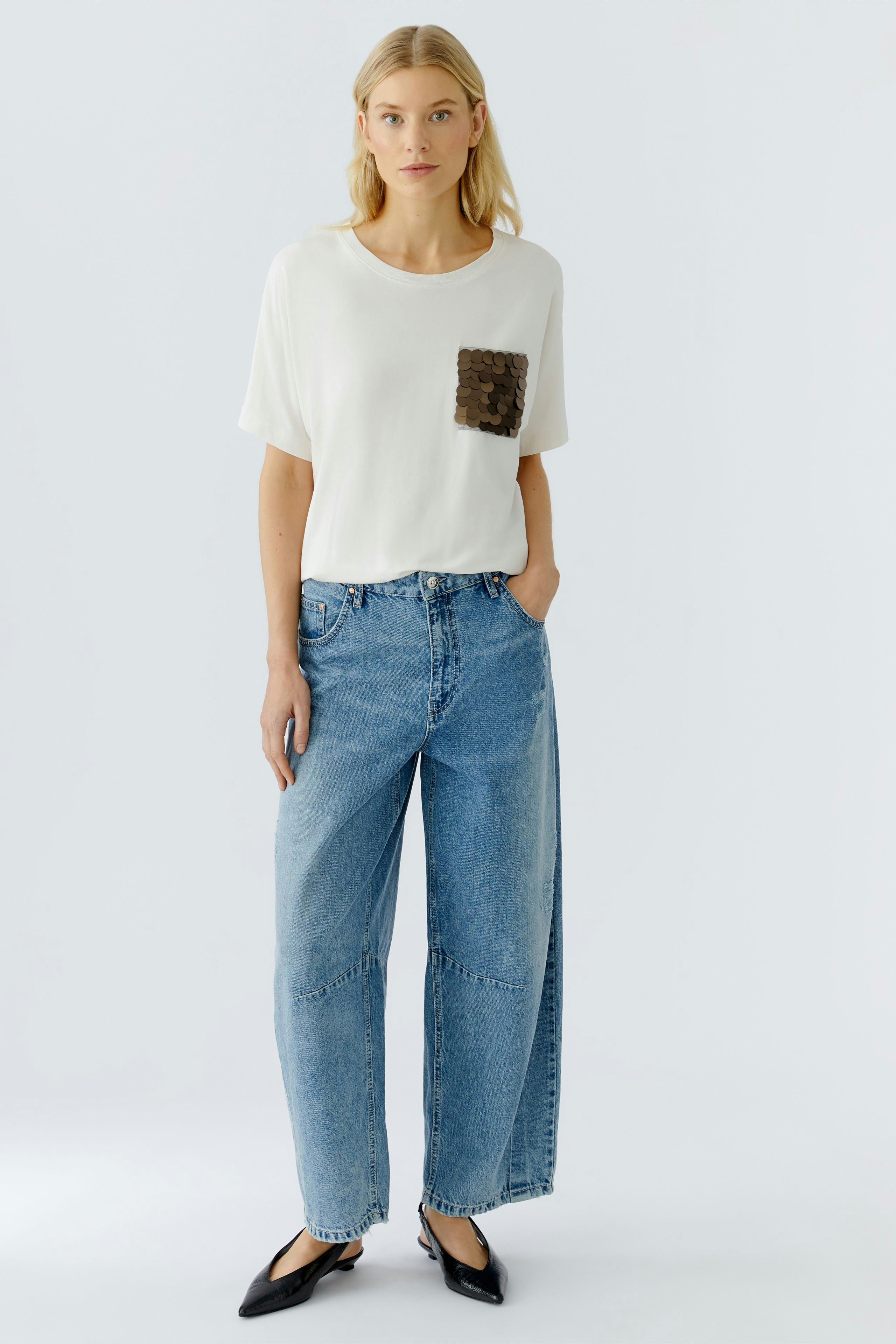 Casual women's T-shirt: Young woman in a white tee with a sequined pocket, paired with wide jeans.