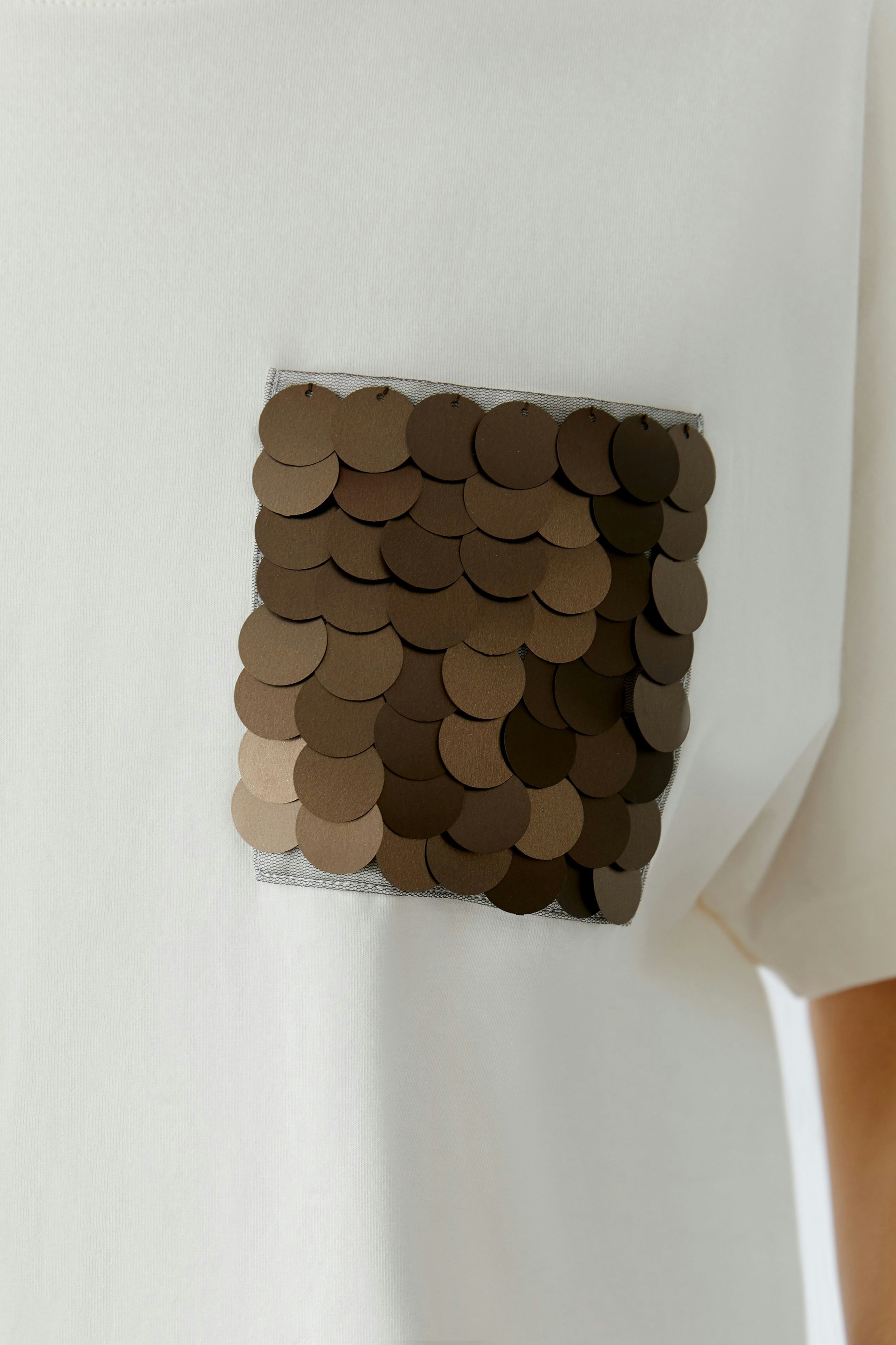 Casual women's T-shirt: Close-up of a white shirt with a sequined pocket detail.