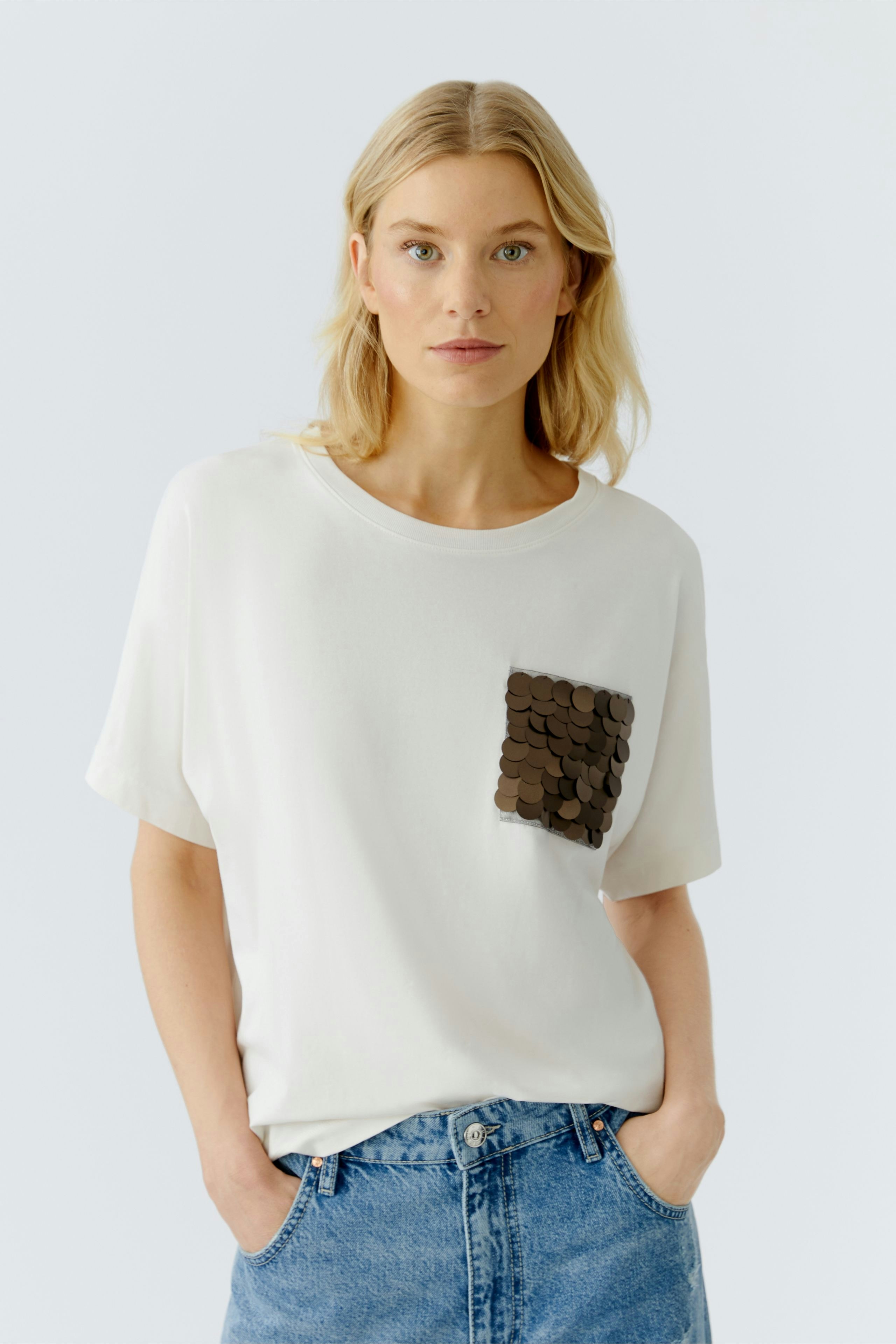 Casual women's T-shirt: Woman in a white tee with a sequined pocket, paired with denim shorts.