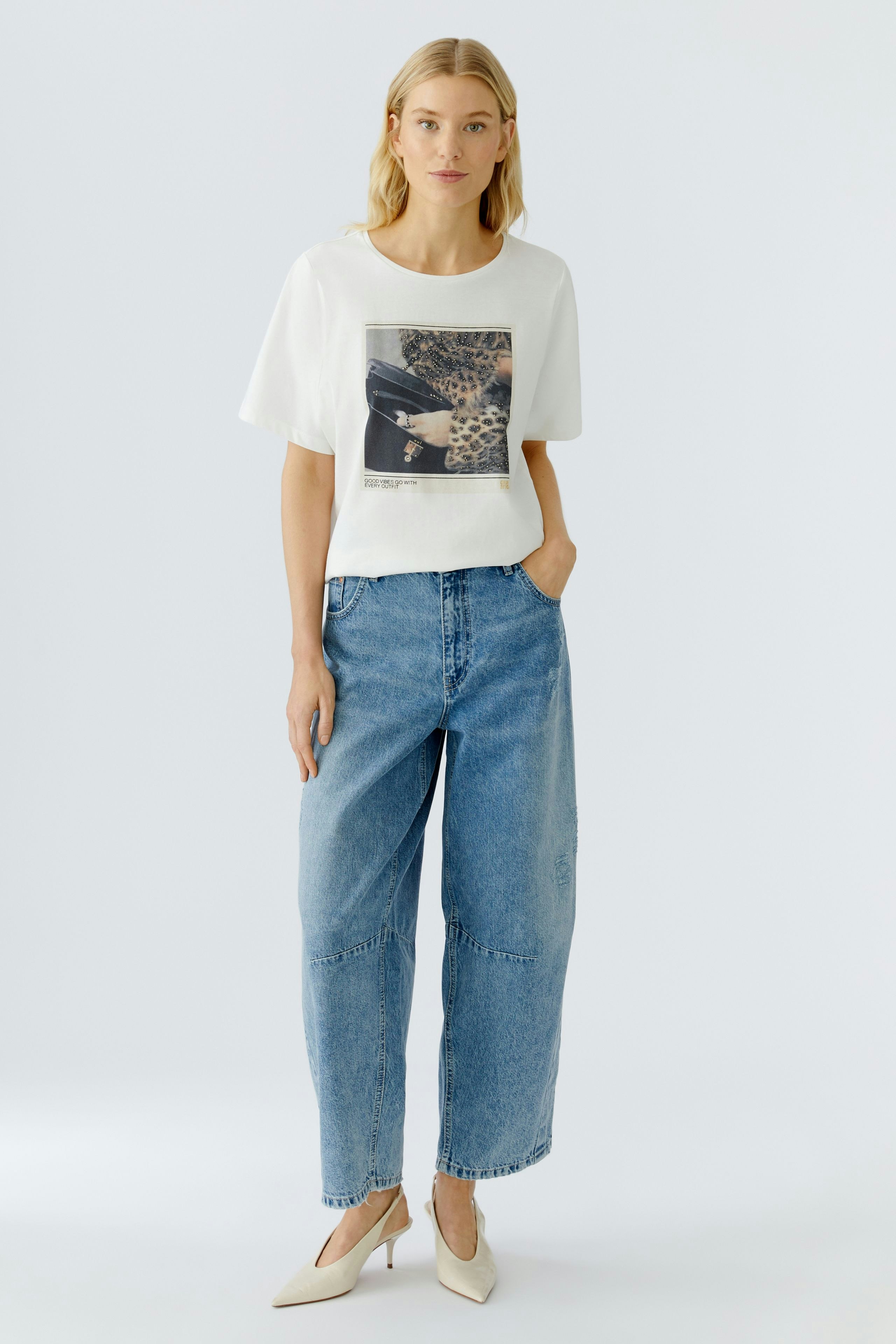 Casual women's T-shirt: Woman in a white tee with a graphic print, paired with relaxed-fit jeans.