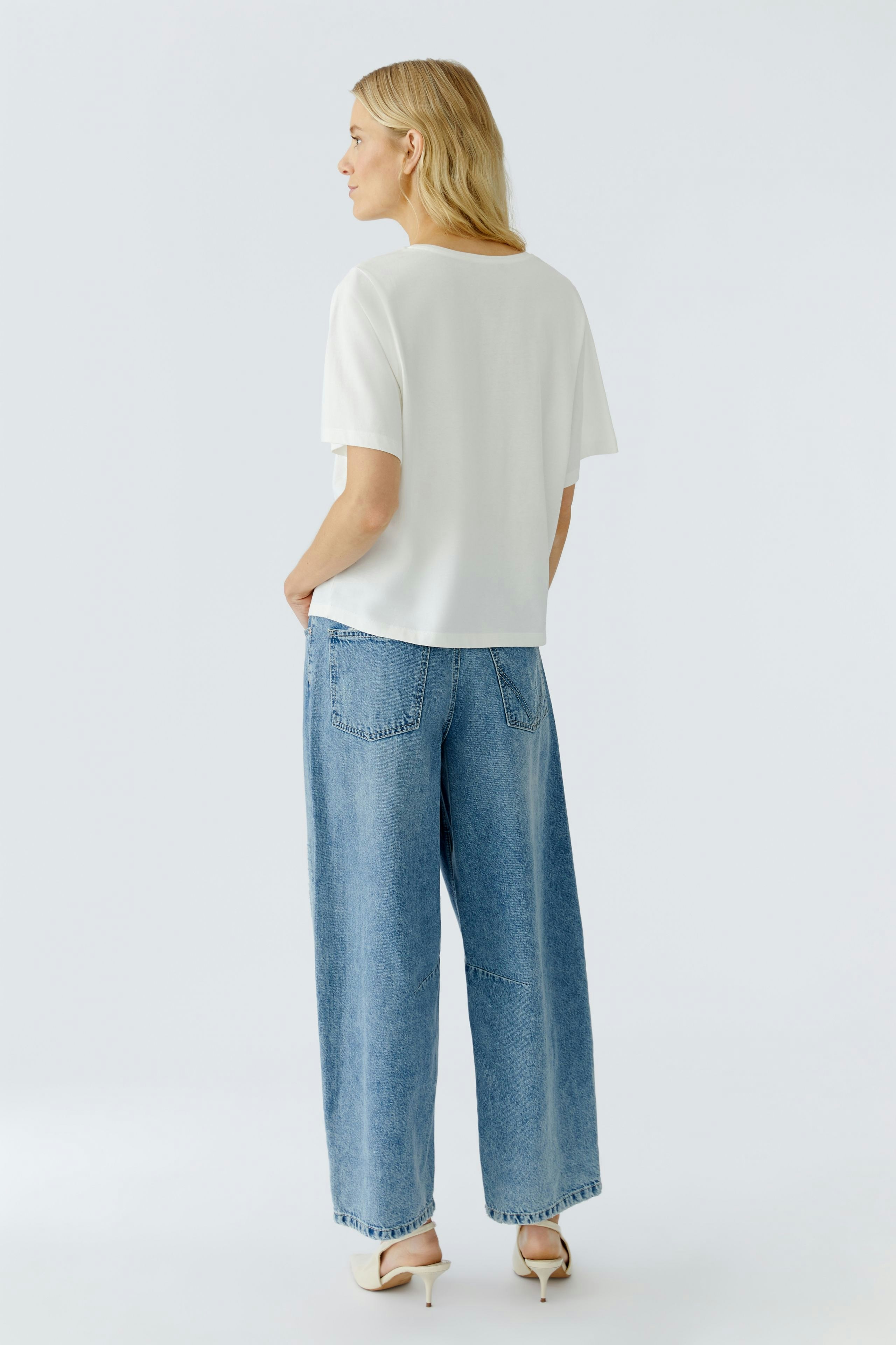 Casual women's T-shirt: A woman in a white T-shirt and wide jeans stands with her back to the camera.
