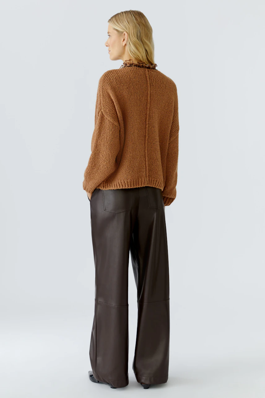 Casual women's pullover: A woman in a cozy brown pullover with a ruffled collar, paired with wide-leg pants.