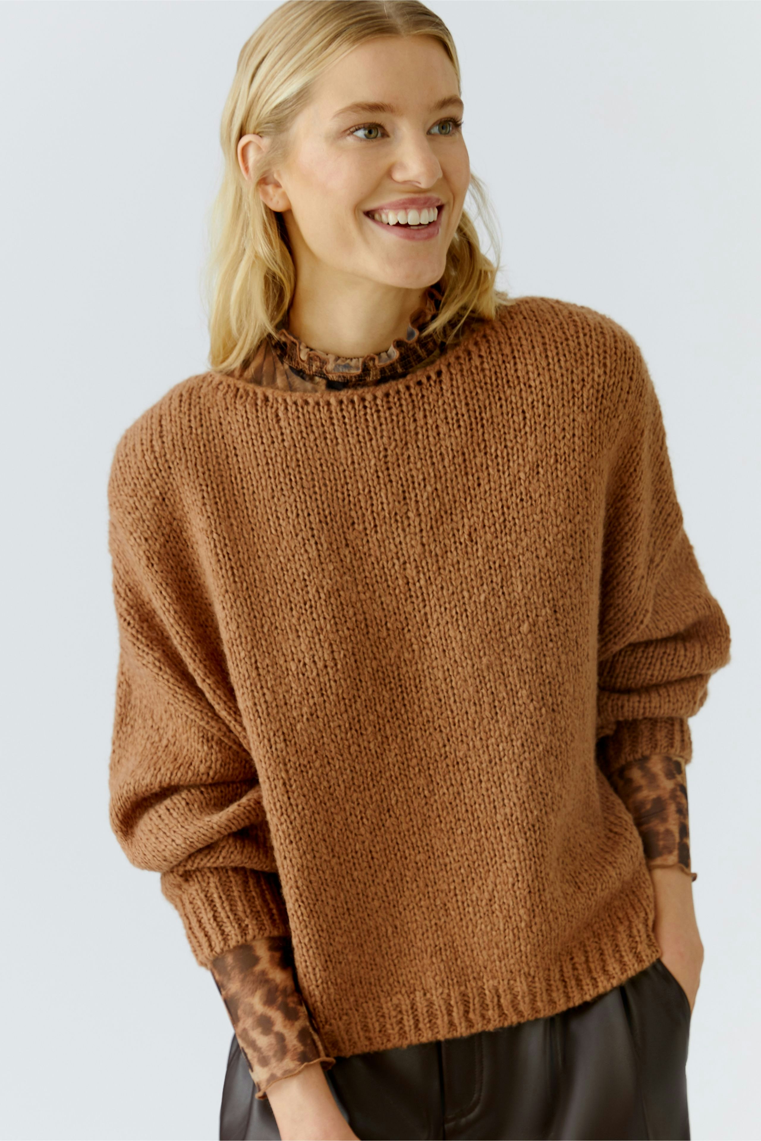 Casual women's pullover: Smiling woman in a cozy brown knit pullover over a patterned top.