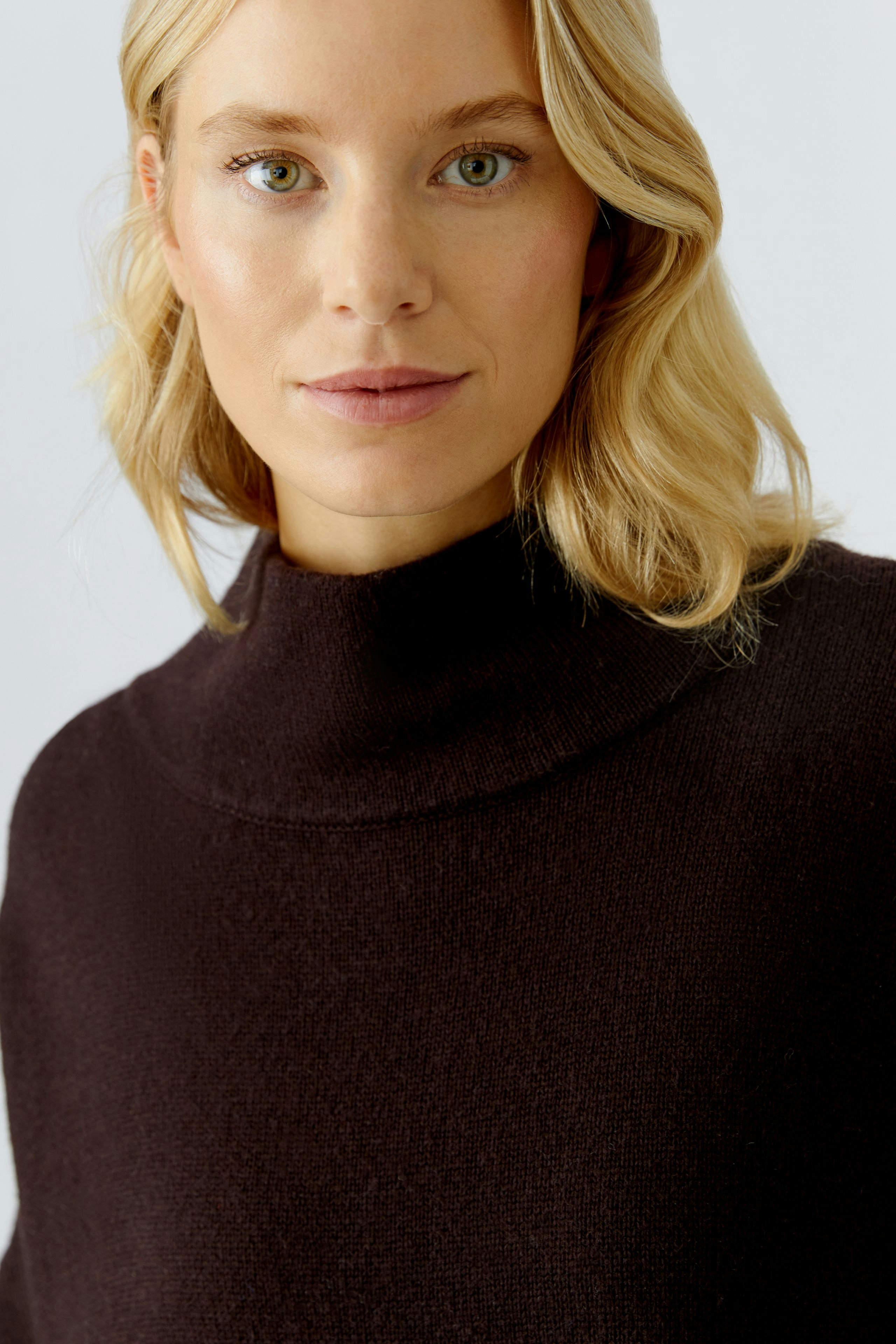 Casual women's pullover: A woman in a dark brown pullover with a high collar, looking confidently at the camera.