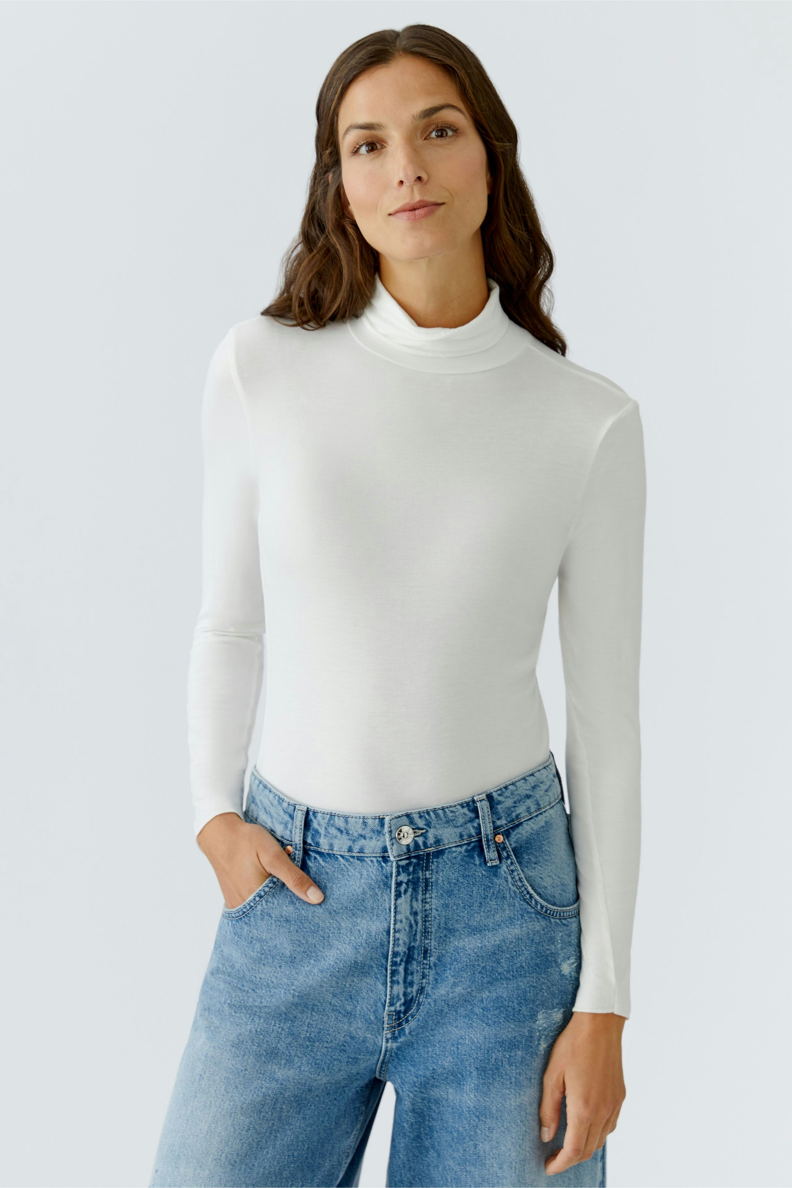 Casual women's long-sleeve shirt: Woman in a white turtleneck top paired with relaxed-fit jeans.