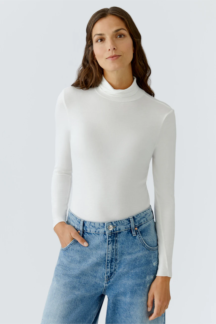 Casual women's long-sleeve shirt: Woman in a white turtleneck top paired with relaxed-fit jeans.