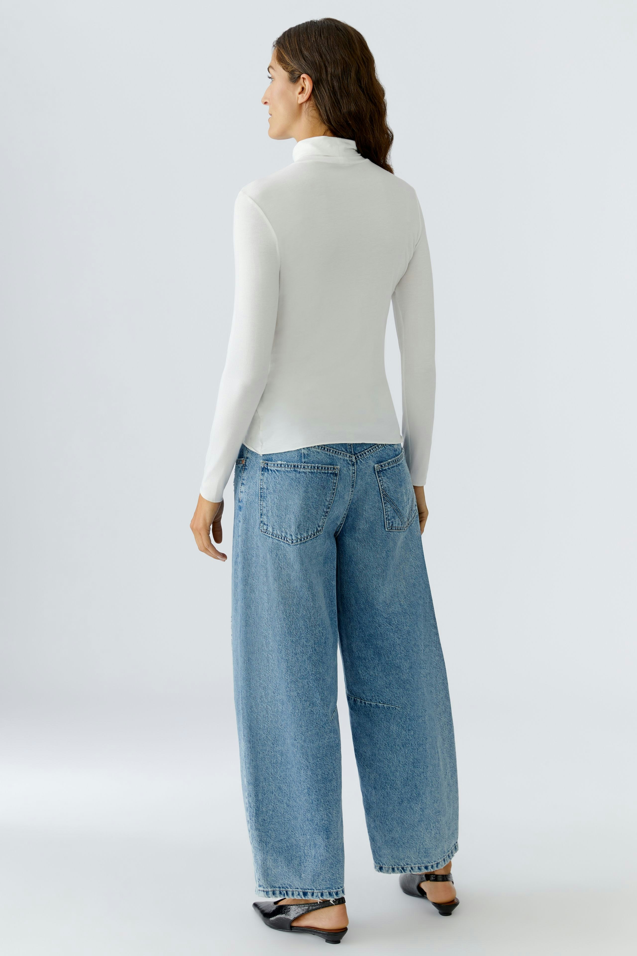 Casual women's long-sleeve shirt: A woman in a fitted white top paired with relaxed blue jeans.