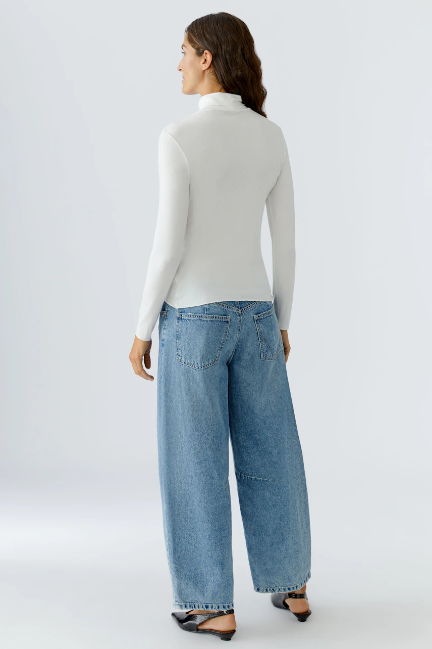 Casual women's long-sleeve shirt: A woman in a fitted white top paired with relaxed blue jeans.