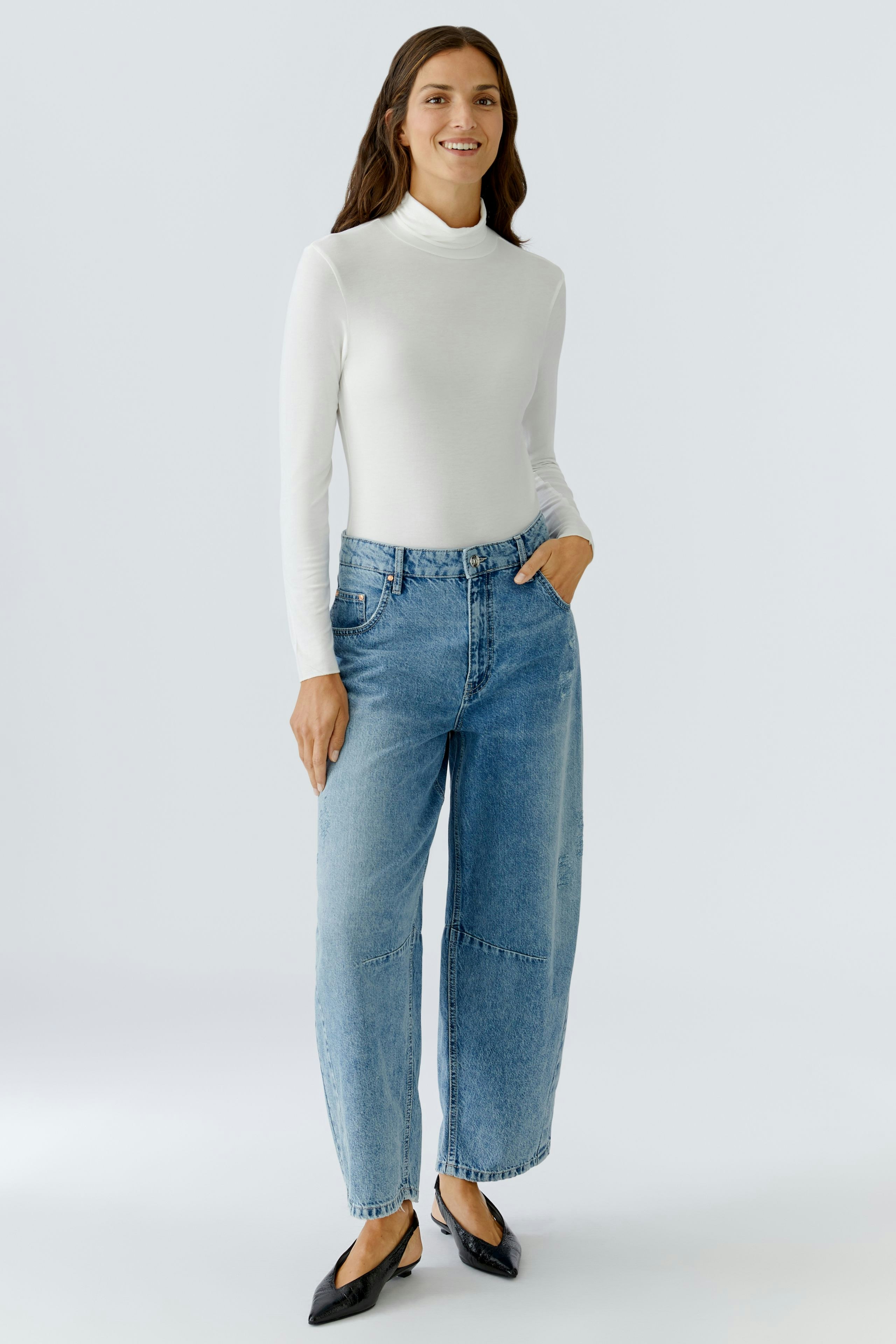 Long-sleeve shirt: Woman in a white fitted pullover paired with relaxed blue jeans.