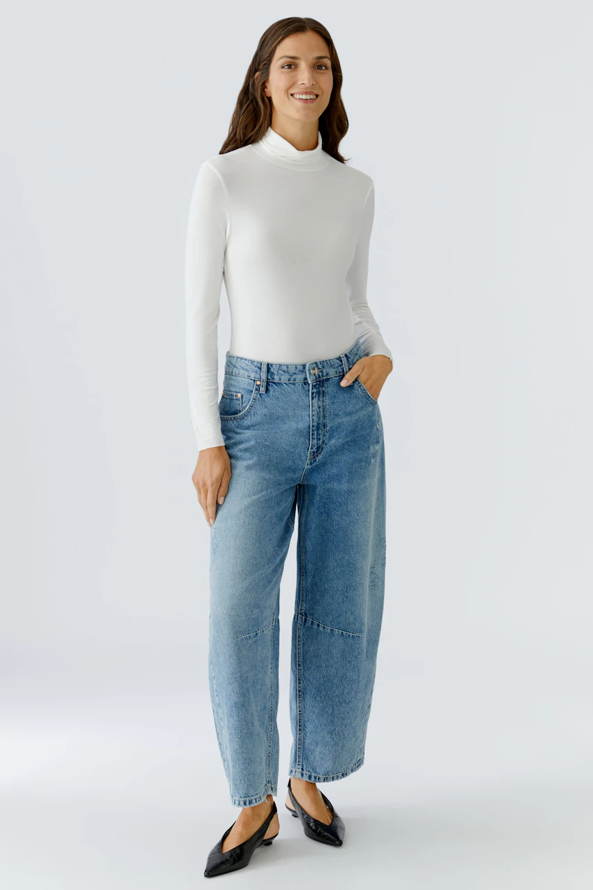 Long-sleeve shirt: Woman in a white fitted pullover paired with relaxed blue jeans.
